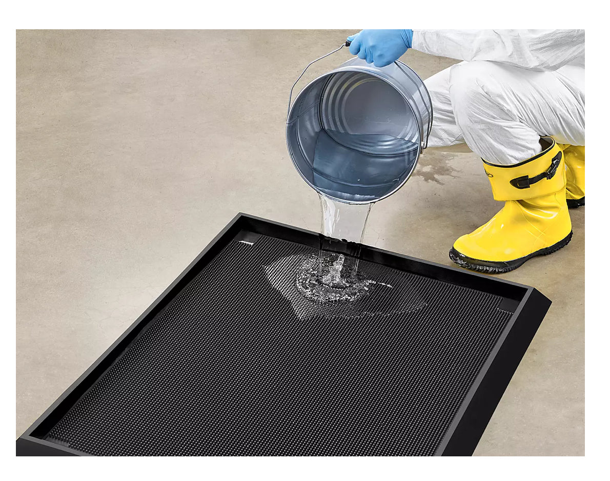 Person in protective gear pouring sanitising liquid onto a black mat from a bucket.