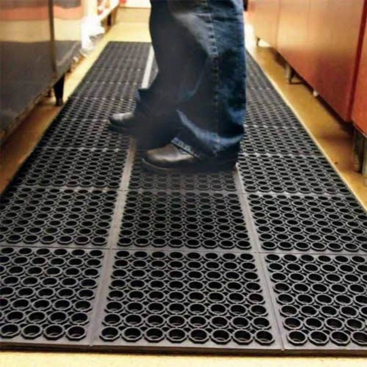 A person walking on a black perforated rubber mat in a store.