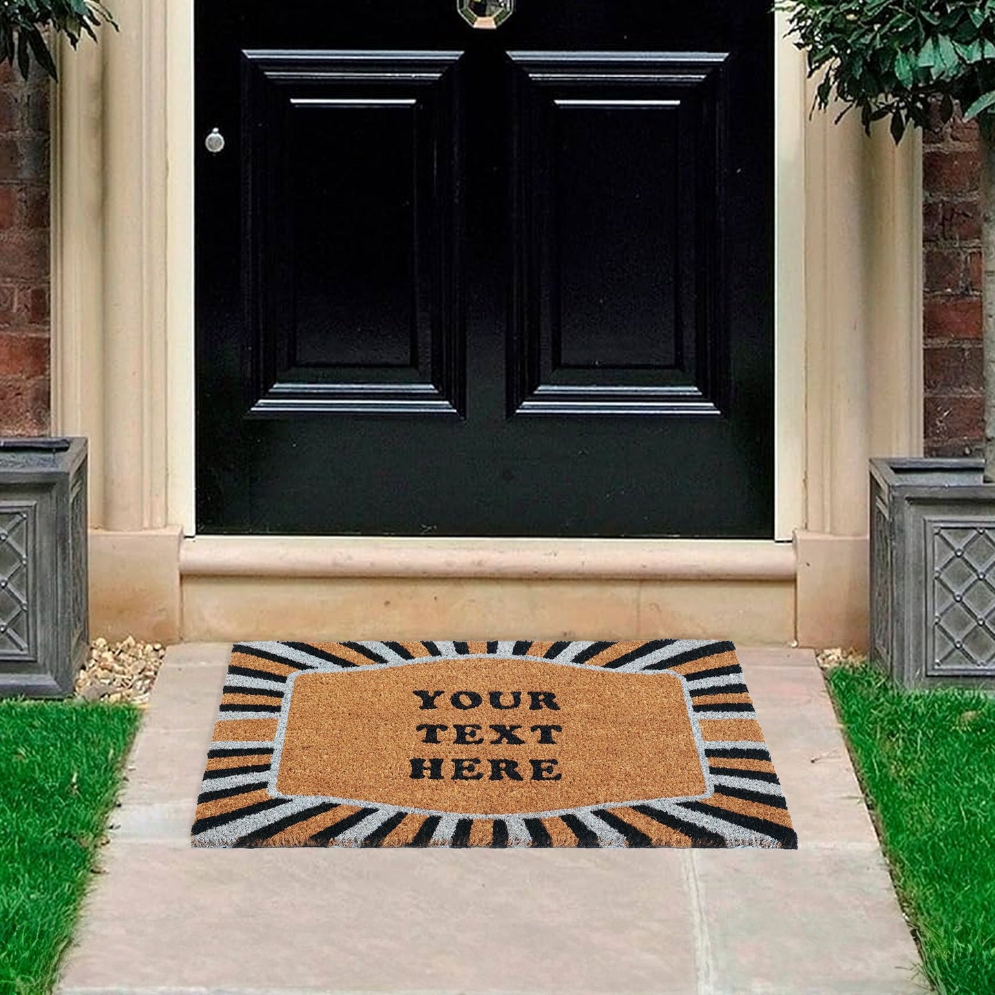 A customizable coir doormat with a personalized text area and a decorative sunburst border, placed on the entrance steps of a house.