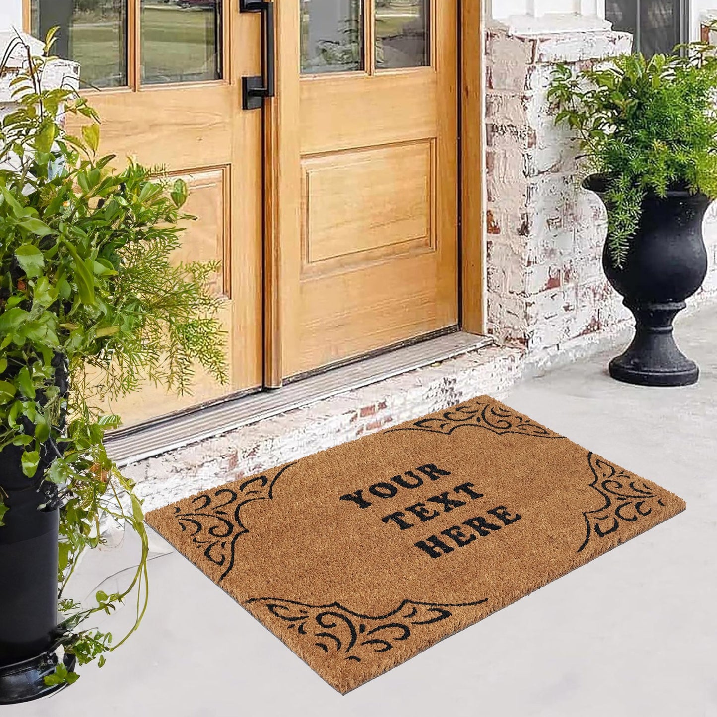 A personalised coir doormat with floral border design and custom text 'Your Text Here' printed in the centre, placed on the doorstep of a home with a brick wall and potted plants in the background.
