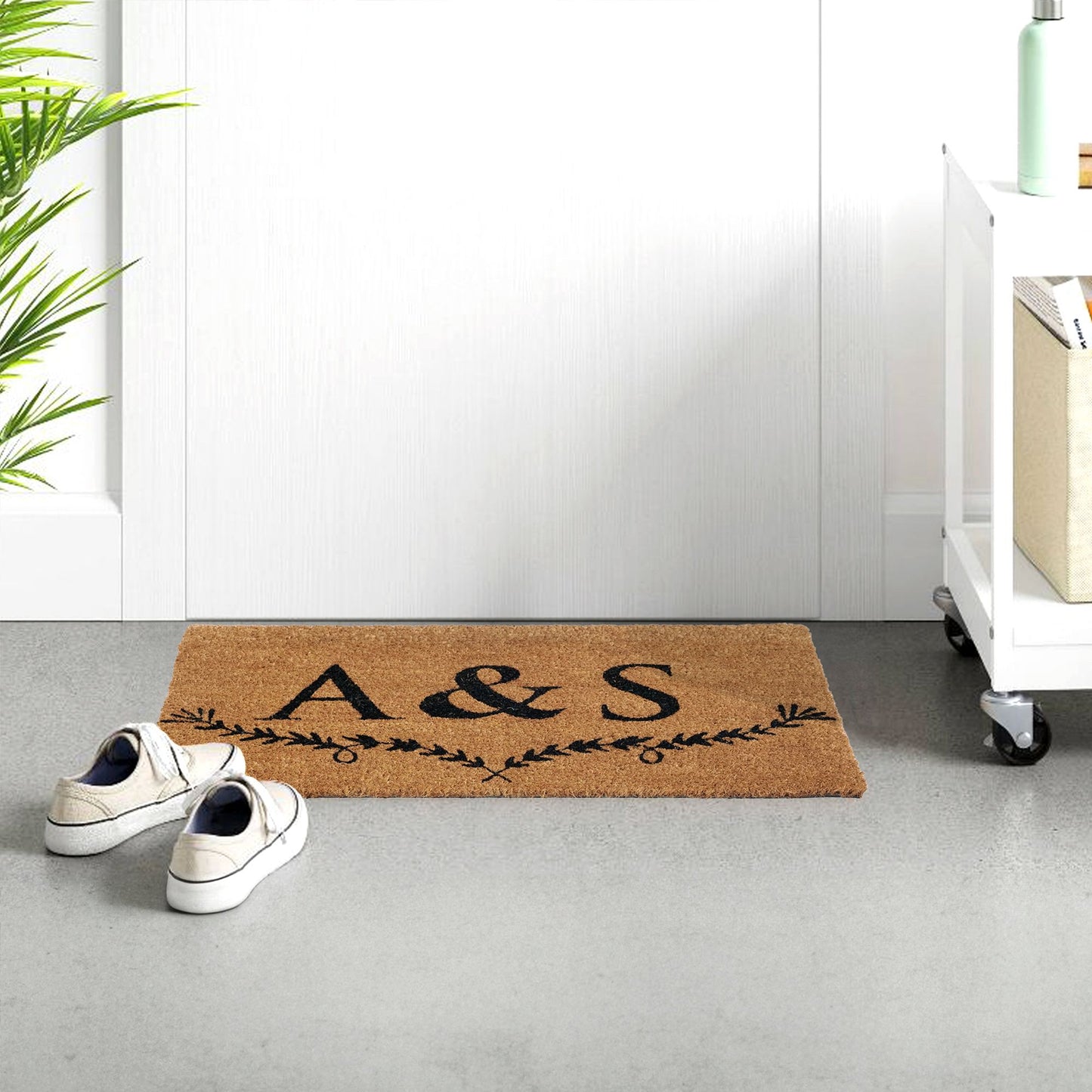 A personalised coir doormat with the initials 'A&S' embossed on it, placed on the floor next to a white door, with a pair of shoes at the bottom of the image.