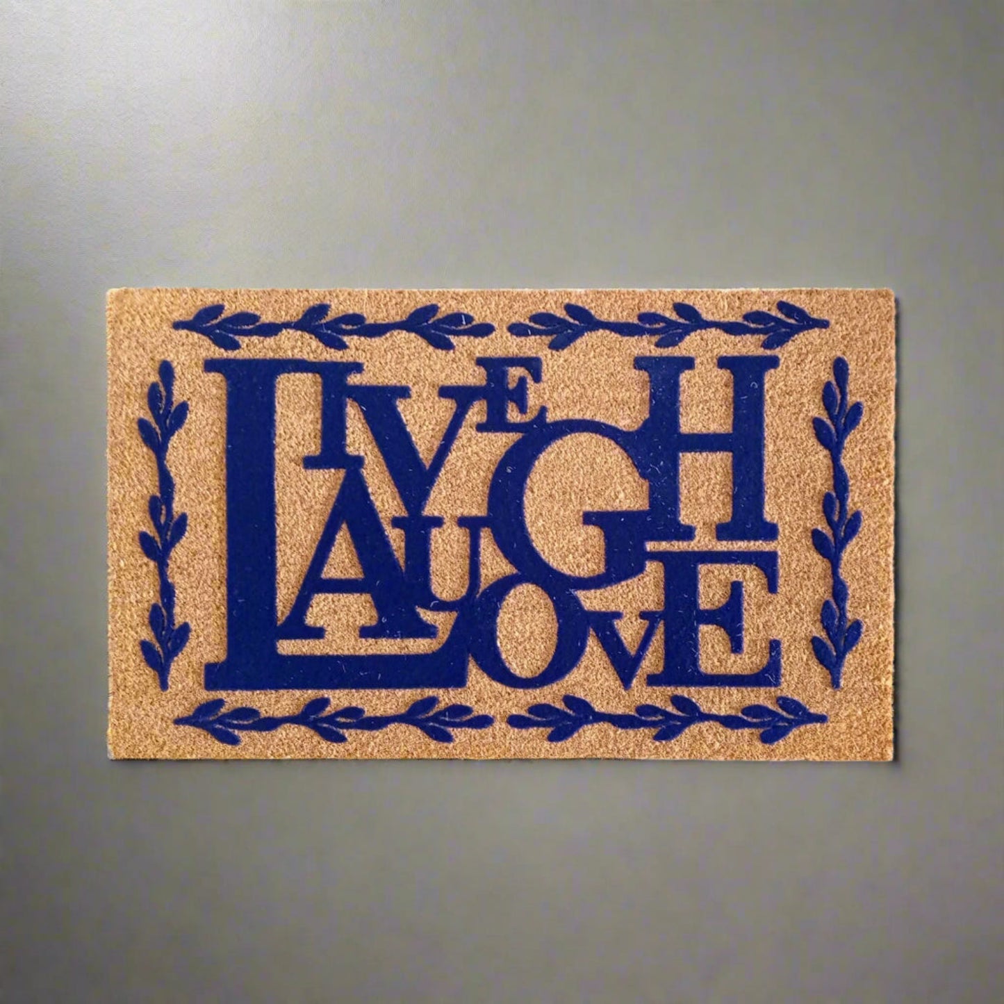 Rectangular coir entrance doormat with the inscription 'Live Laugh Love' in bold blue letters, surrounded by a floral wreath design.