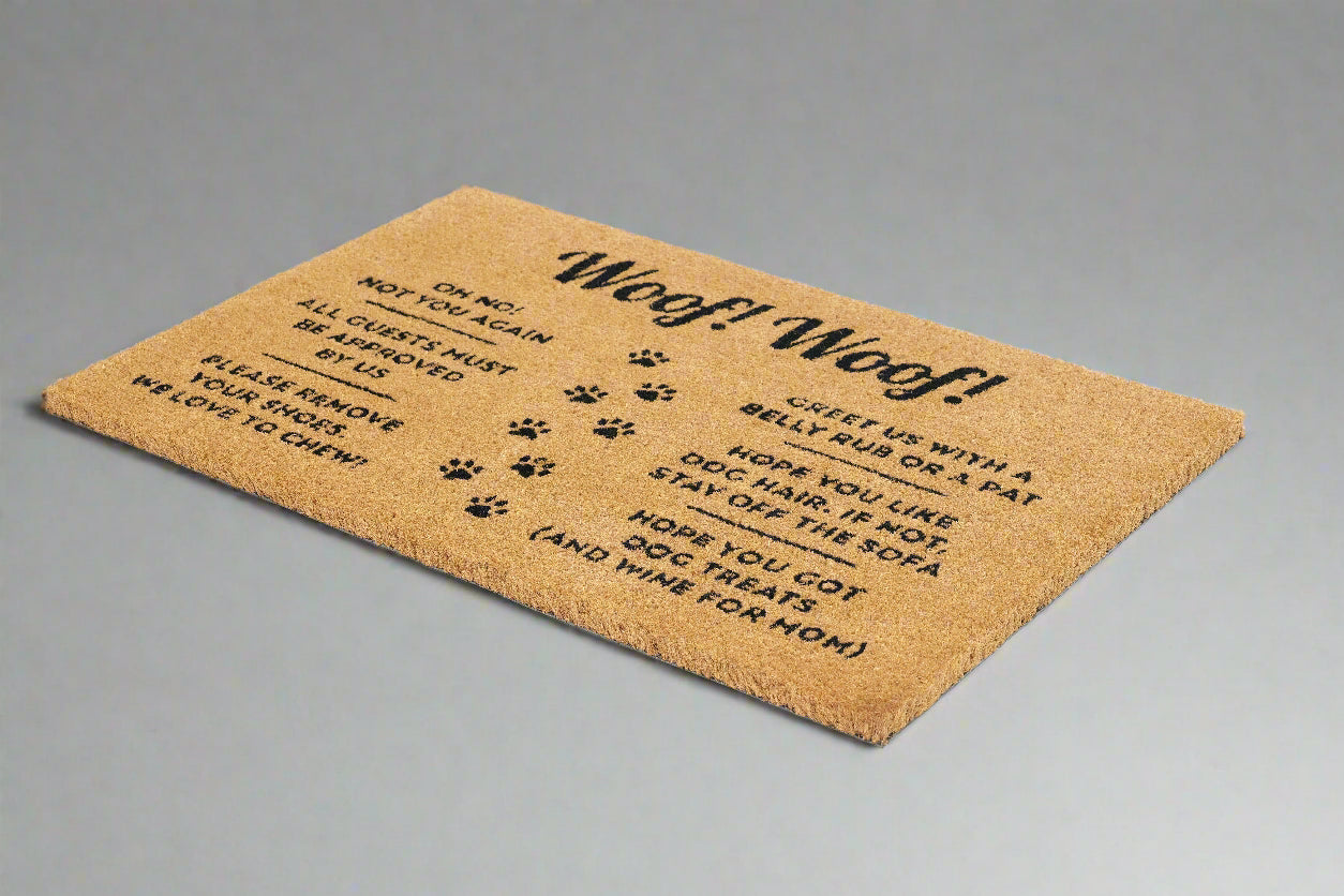 A rectangular natural coir doormat with a dog-themed design, featuring text and paw prints, on a white background.