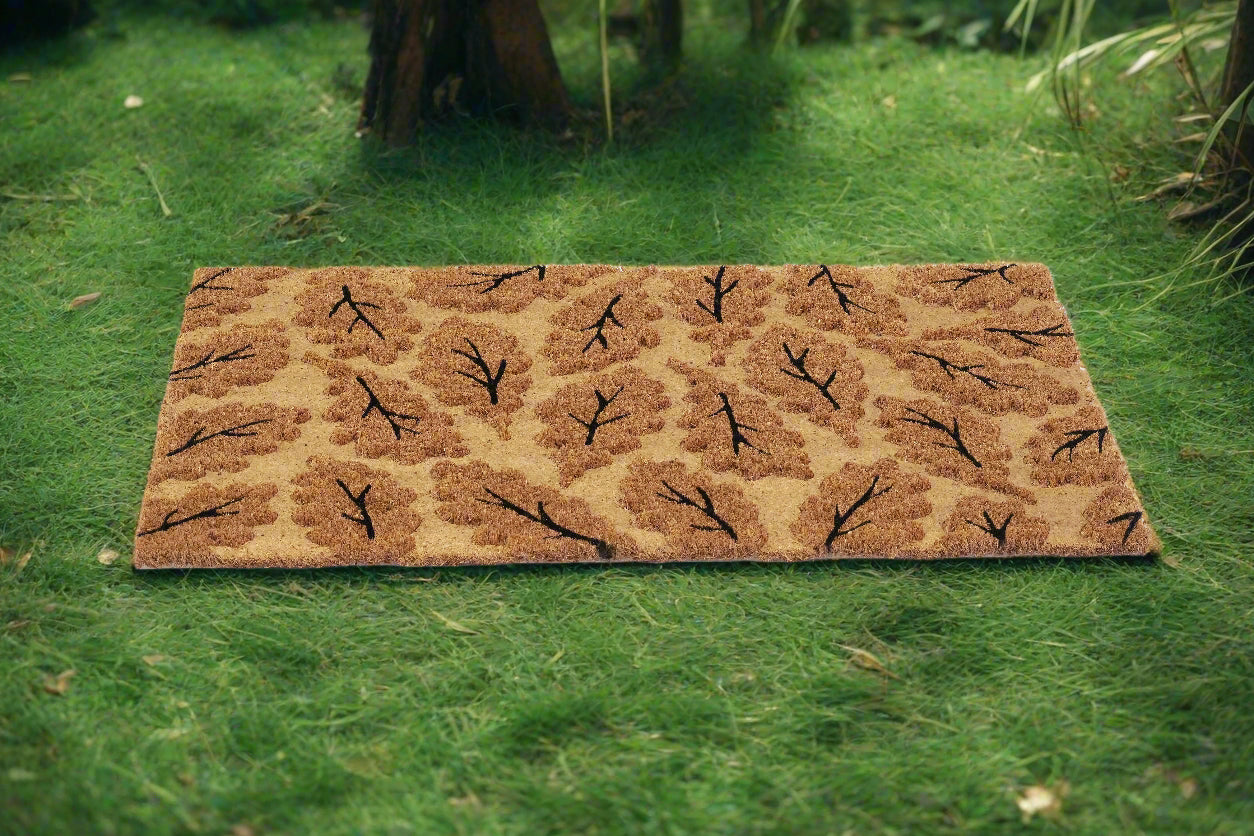 A beige coir mat with a leaf impression printed design, placed on a grassy surface.