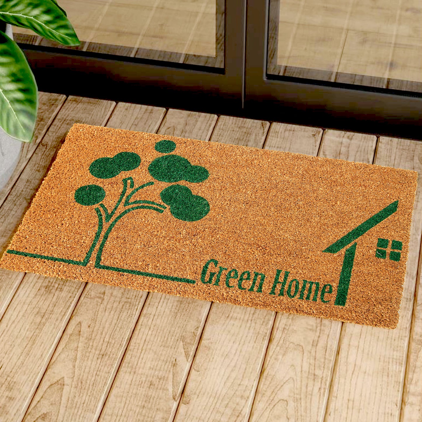 Rectangular coir doormat with a green tree and house design, placed on a wooden floor, with a plant in the background.