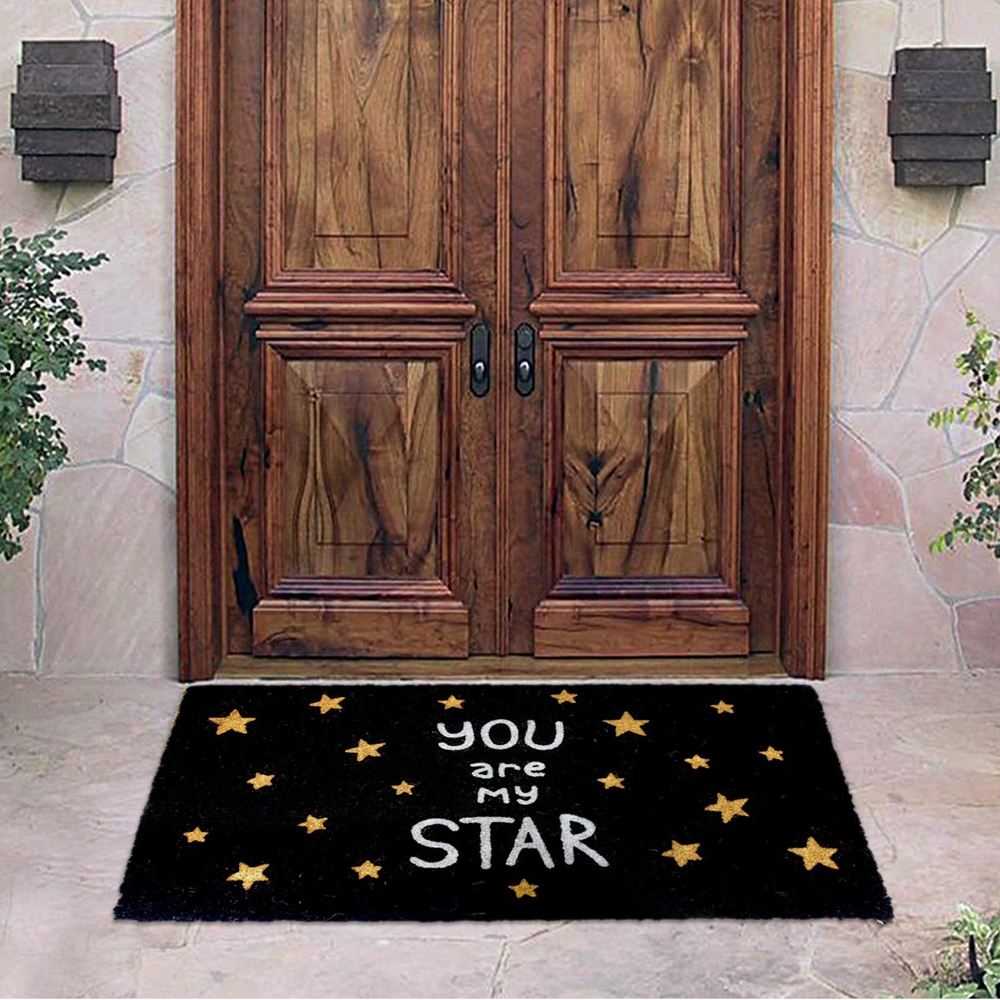 A black glitter-printed doormat with the text 'You are My Star' and star shapes on it, placed on the floor in front of a wooden door.