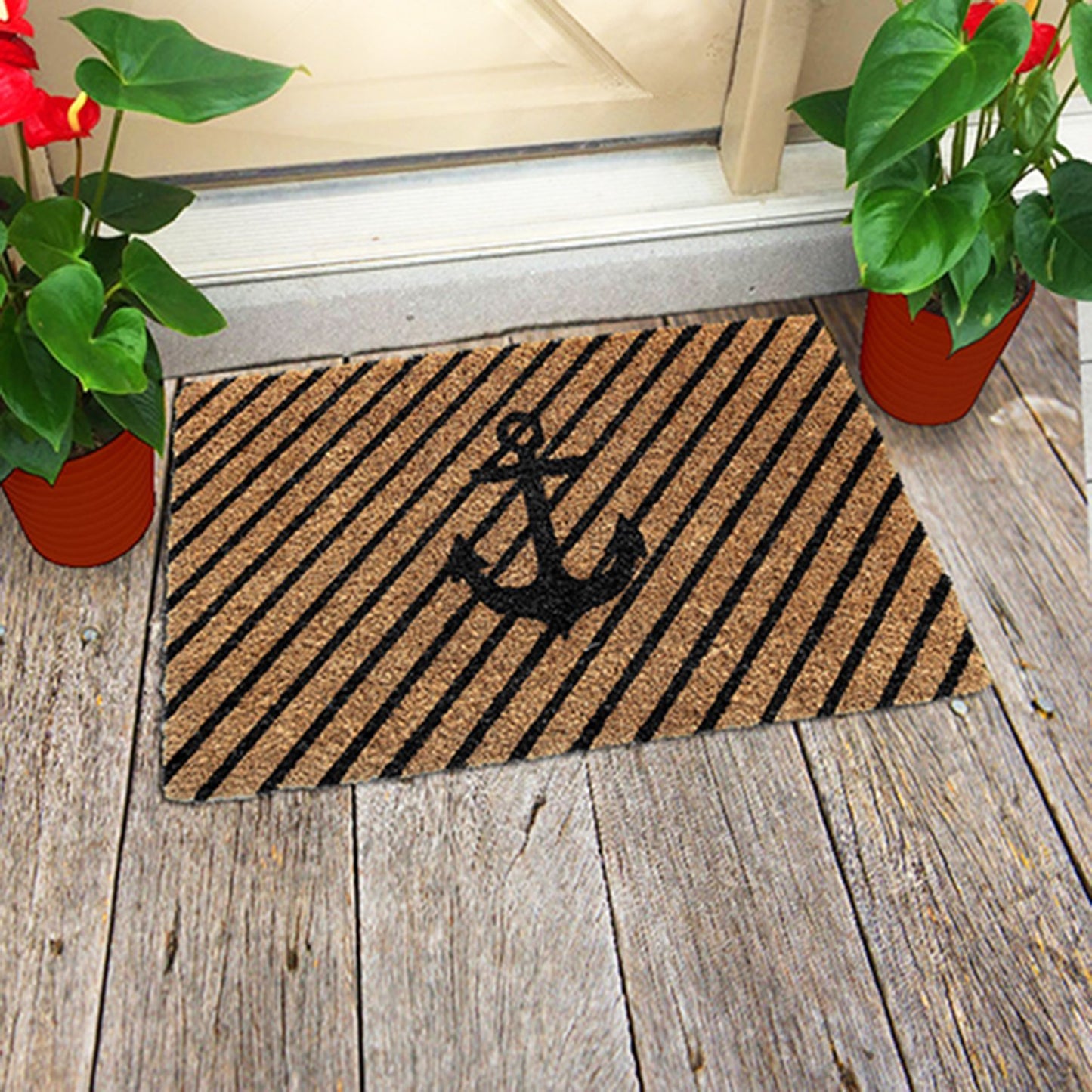 A rectangular natural coir floor mat with a black ship anchor print, placed on a wooden floor by a door, with potted plants on either side.