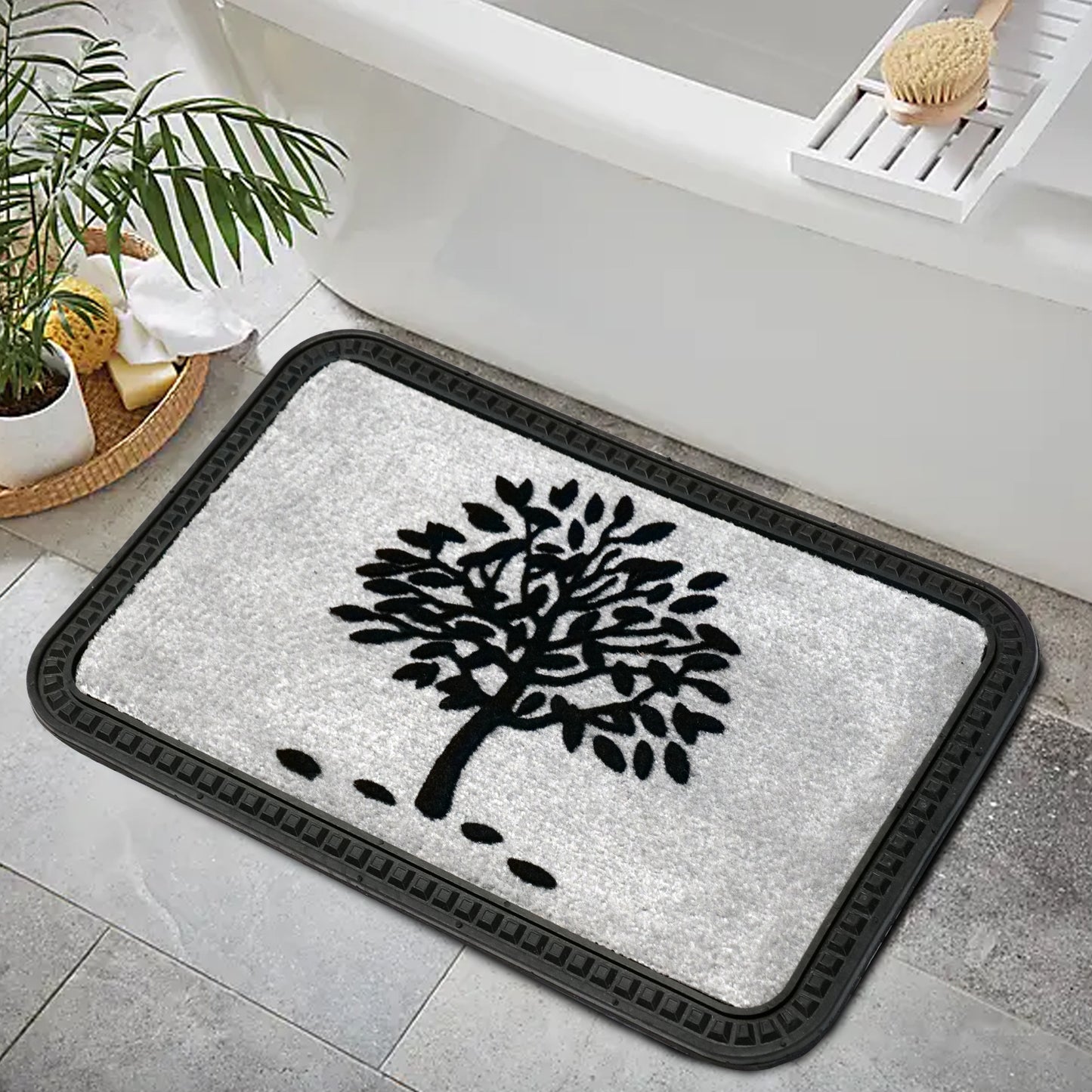 A black rectangular doormat with an ornamental tree design, placed on a bathroom floor with a plant and a wooden object in the background.