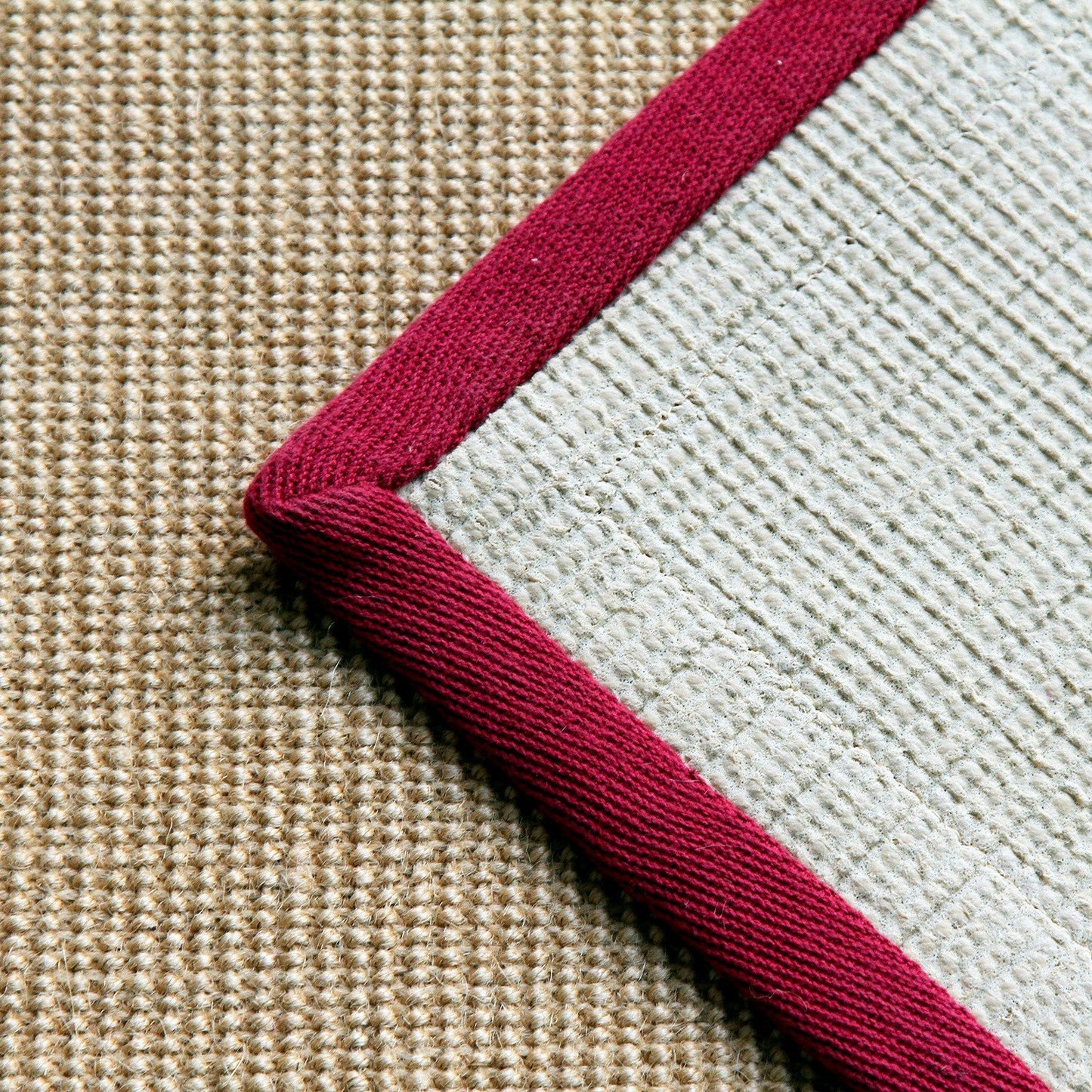 A rolled-up yoga mat with a maroon cotton border and natural jute colour visible in the centre.
