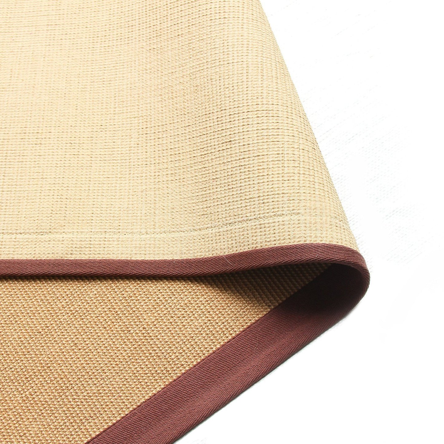 A beige jute yoga mat with a brown cotton border and a small section of the latex backing visible.