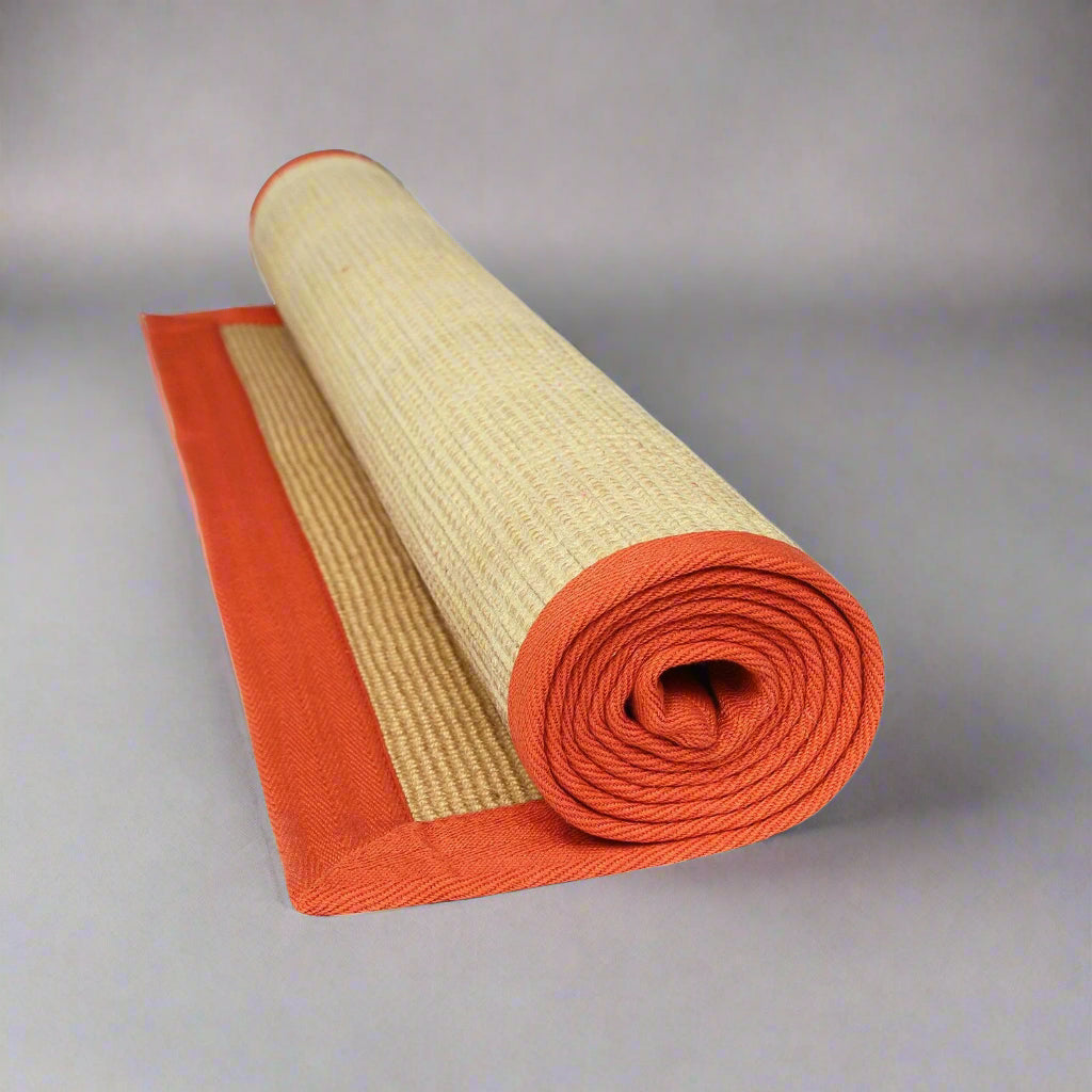 A rolled-up yoga mat with beige jute material and an orange cotton border, placed on a white background.