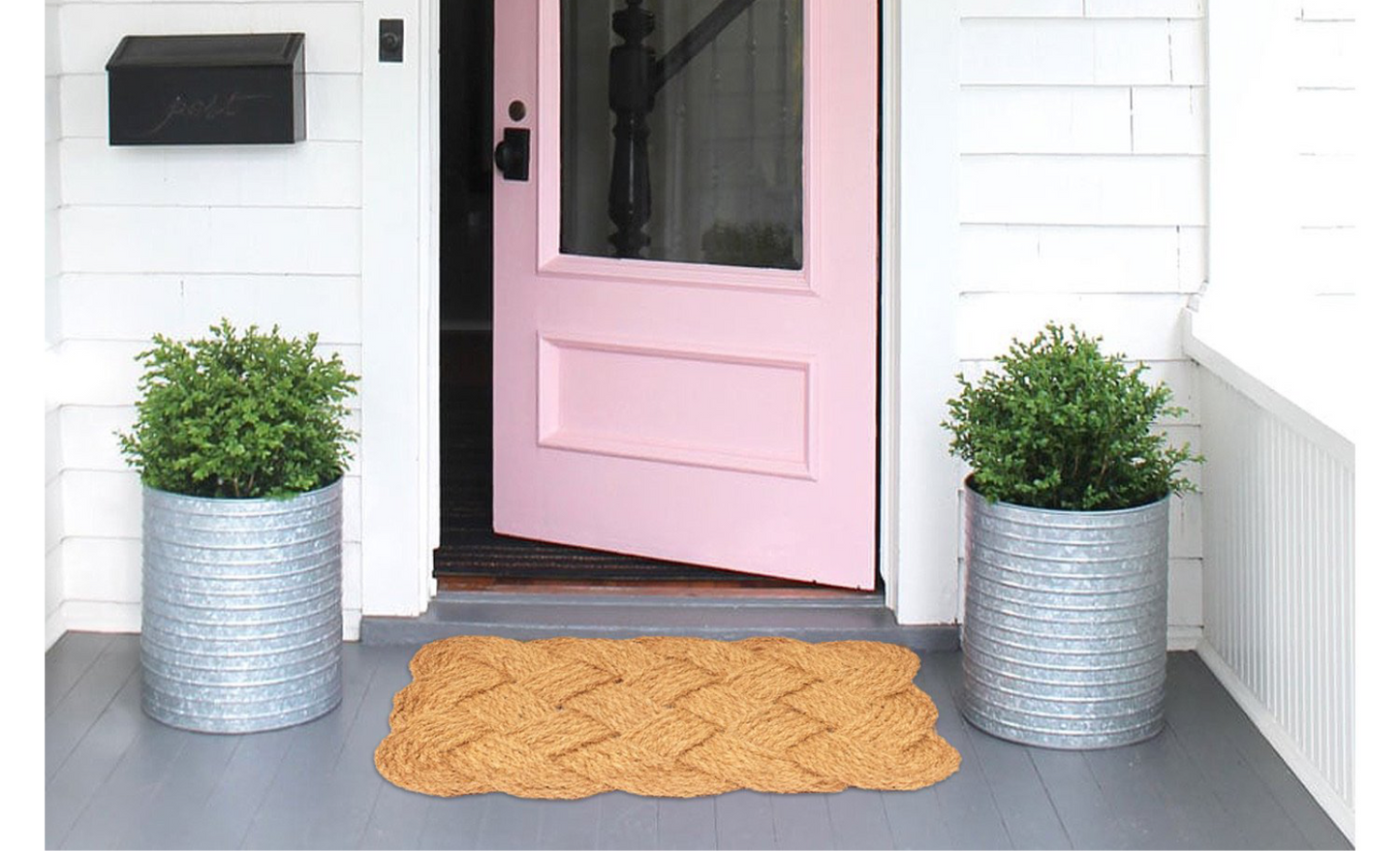 Pink front door with two potted plants and a textured coir doormat on a grey step.