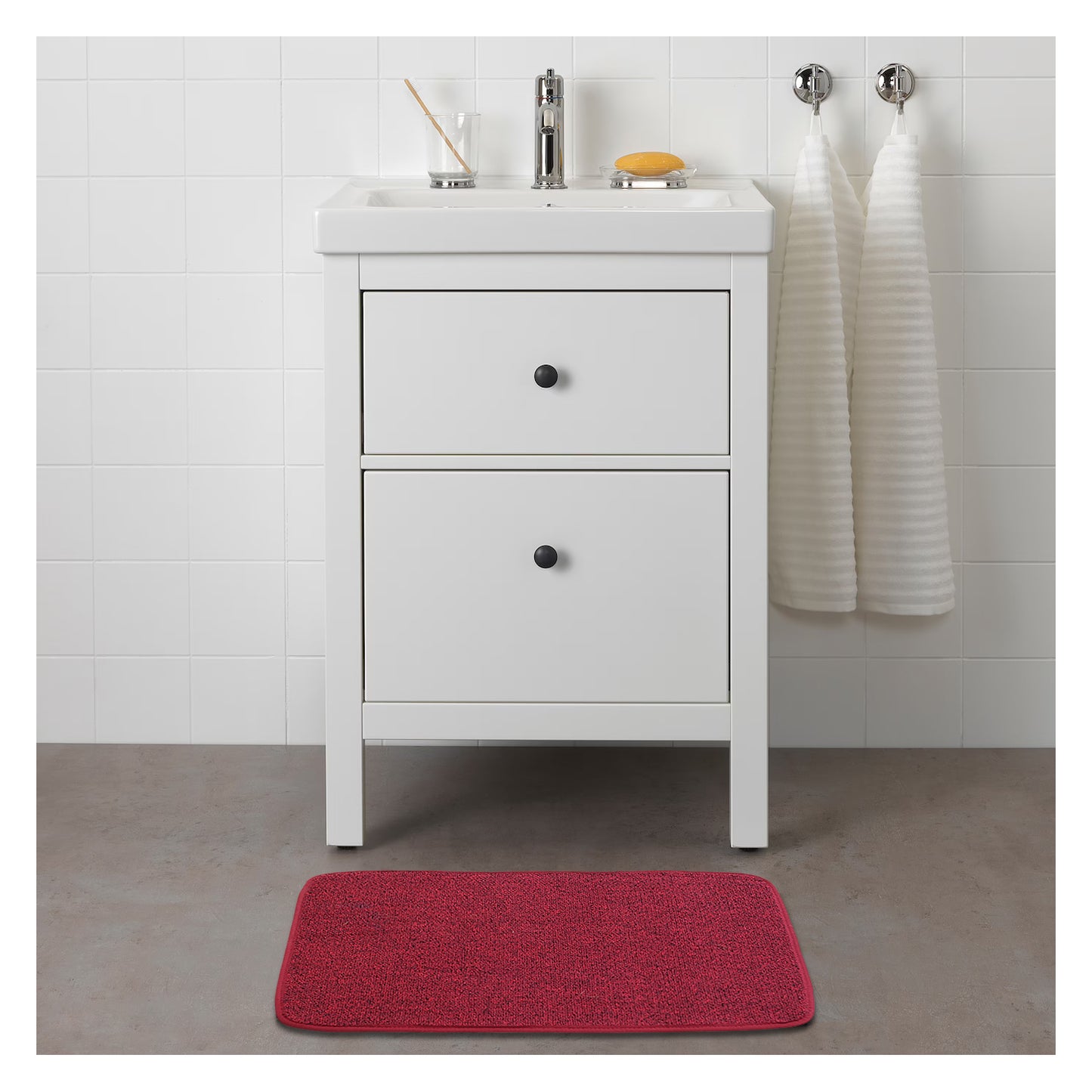A red rectangular mat with a textured surface is placed on the floor in front of a white cabinet.