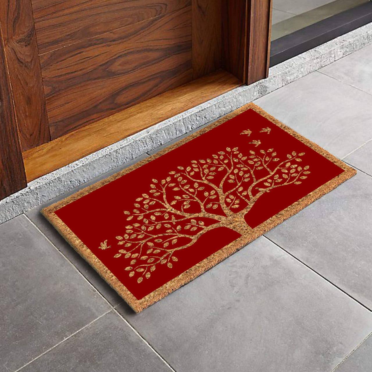 A rectangular natural coir red door mat with a printed Tree of Life and chirping birds design, placed on a tiled floor.