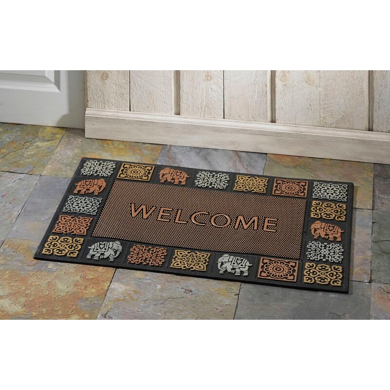 A tri-colored rubber door mat with animal patterns and the word 'WELCOME' in bold letters, placed on a tiled floor next to a wooden door.