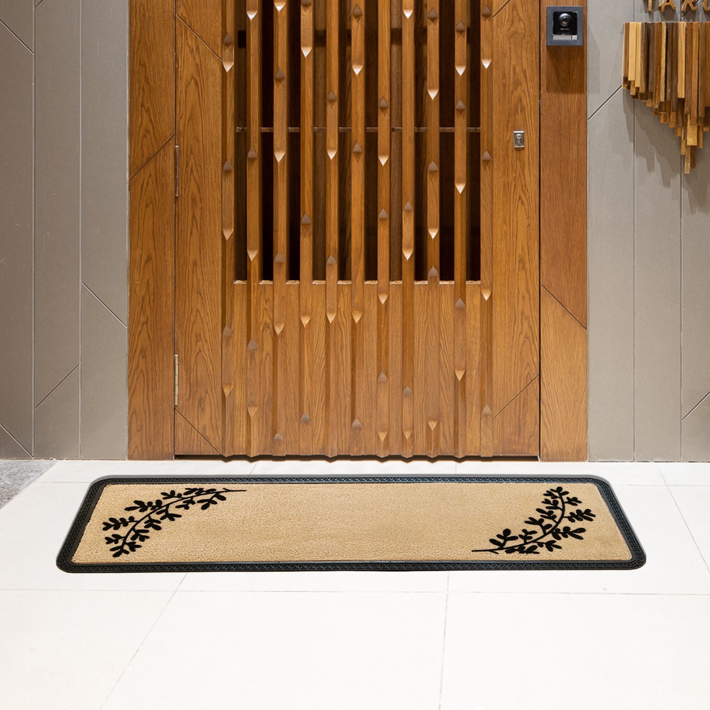 A beige polypropylene flocked floor mat with a leaf pattern placed on a wooden floor near a wooden door.