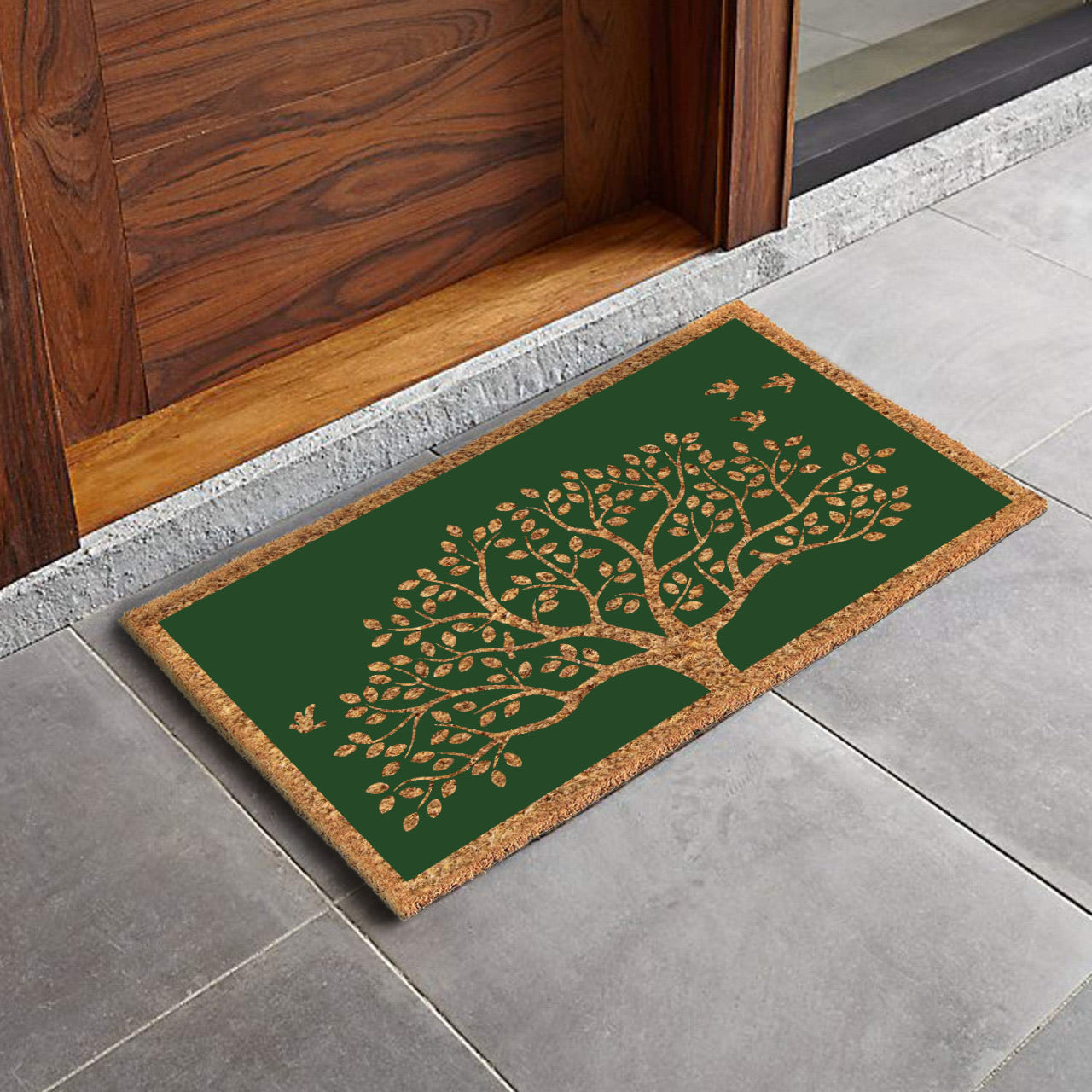 A rectangular natural coir green door mat with a printed Tree of Life and chirping birds design, placed on a tiled floor.