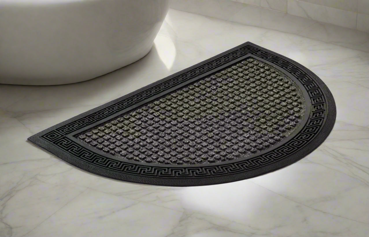 A gray, semi-circular bath mat made of polypropylene with a non-slip base, placed on a tiled bathroom floor.
