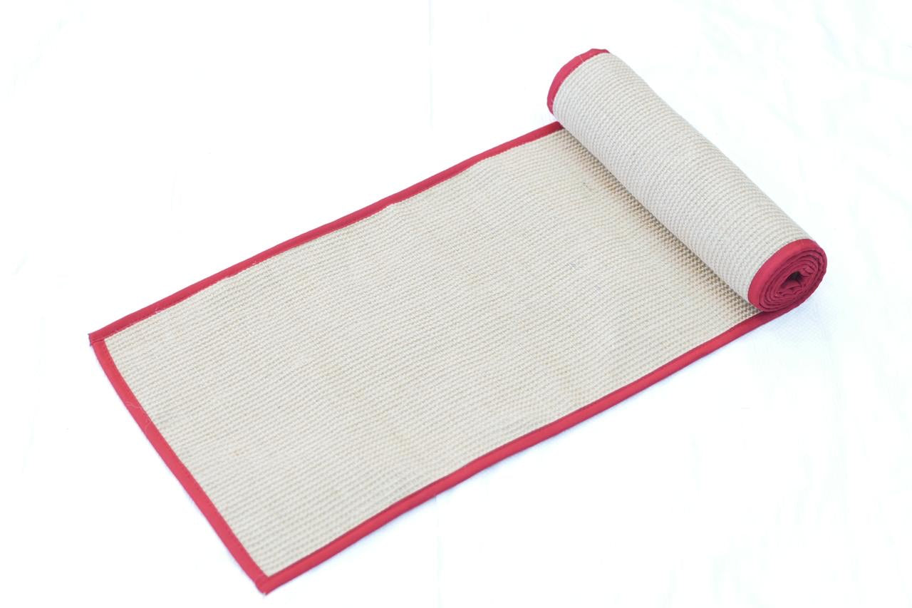 A beige jute table mat with a red cotton border, rolled up with the red border facing up.