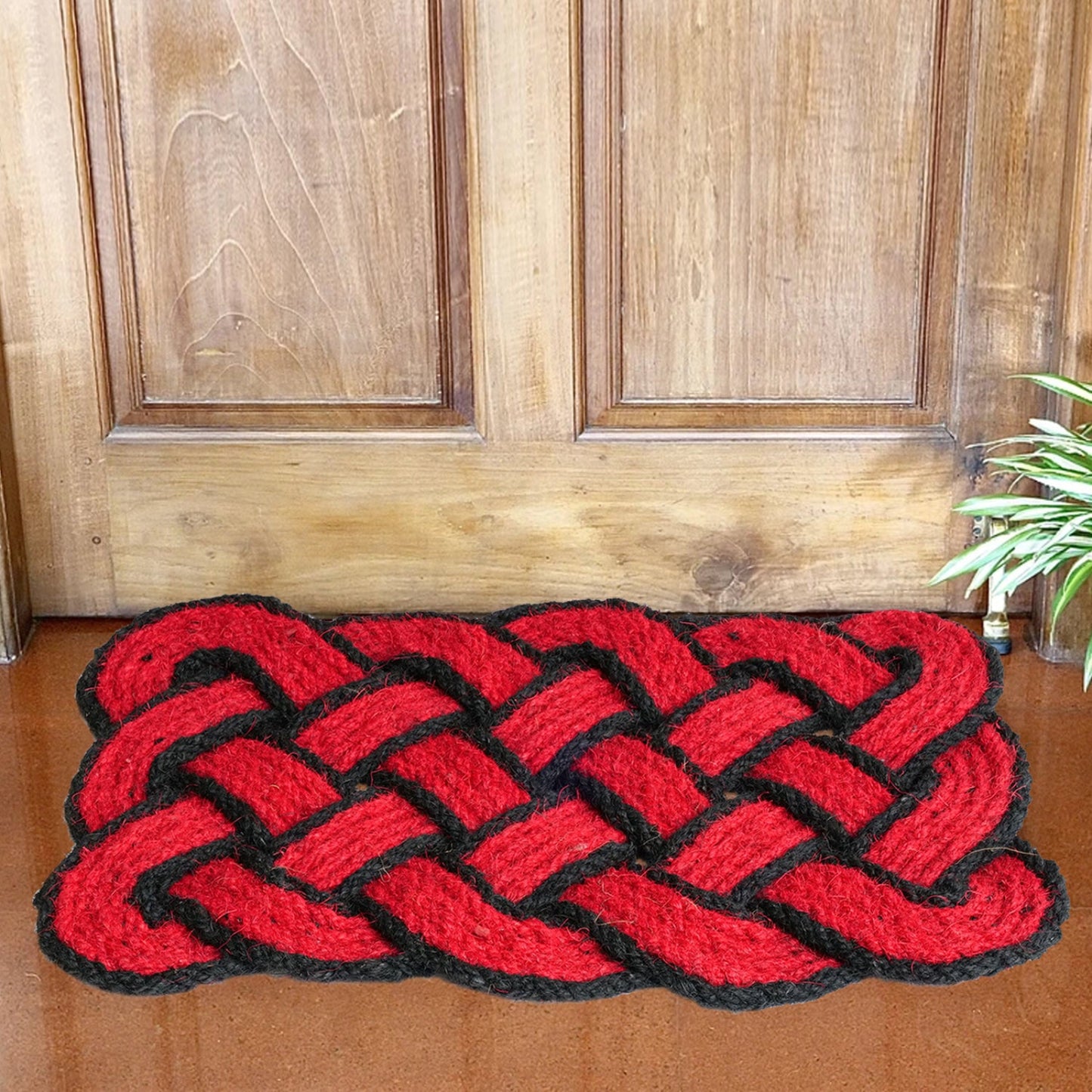 Red braided traditional coir doormat with black edges on a wooden floor.
