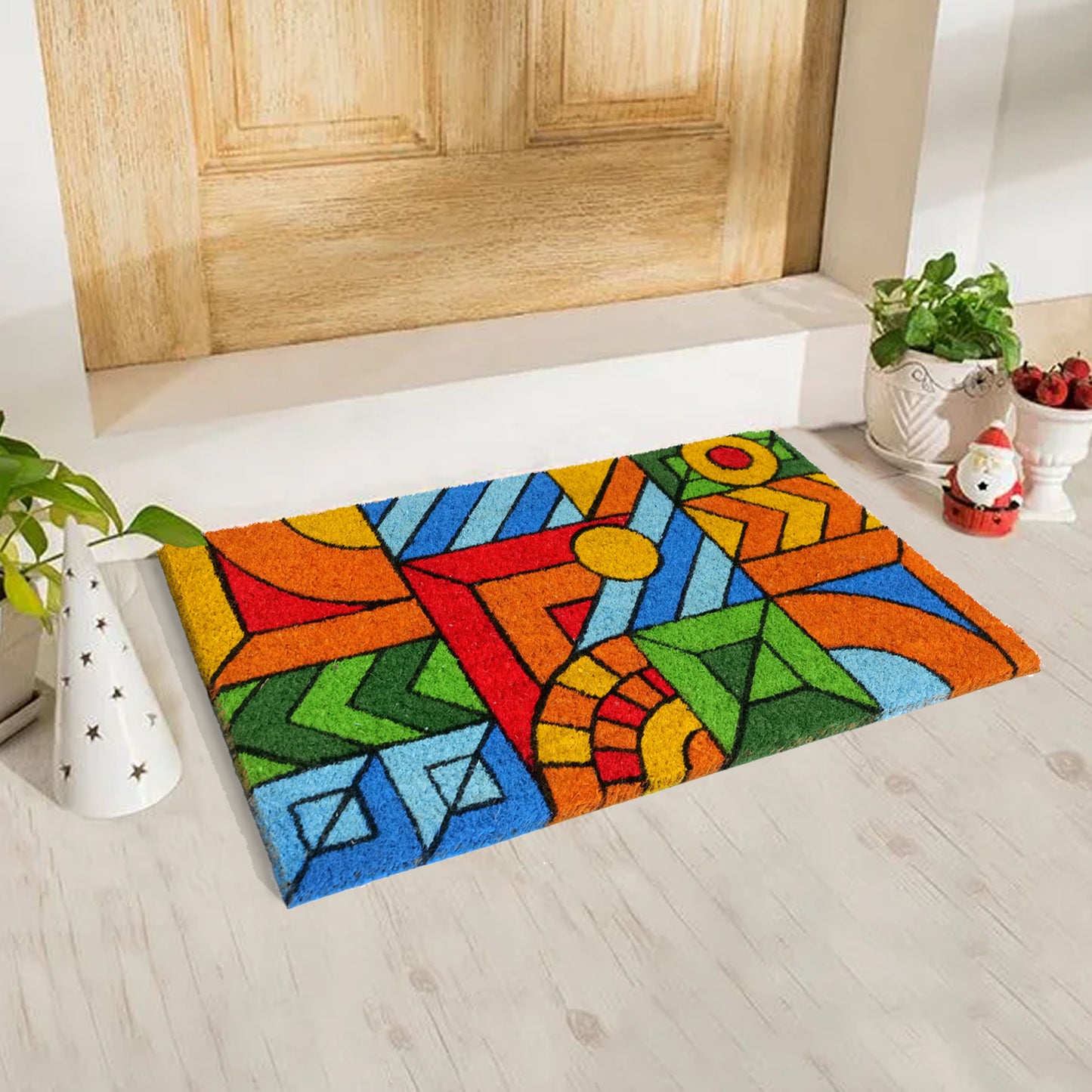 A rectangular natural coir door mat with a colourful geometric pattern, placed on a floor with a wooden door in the background.