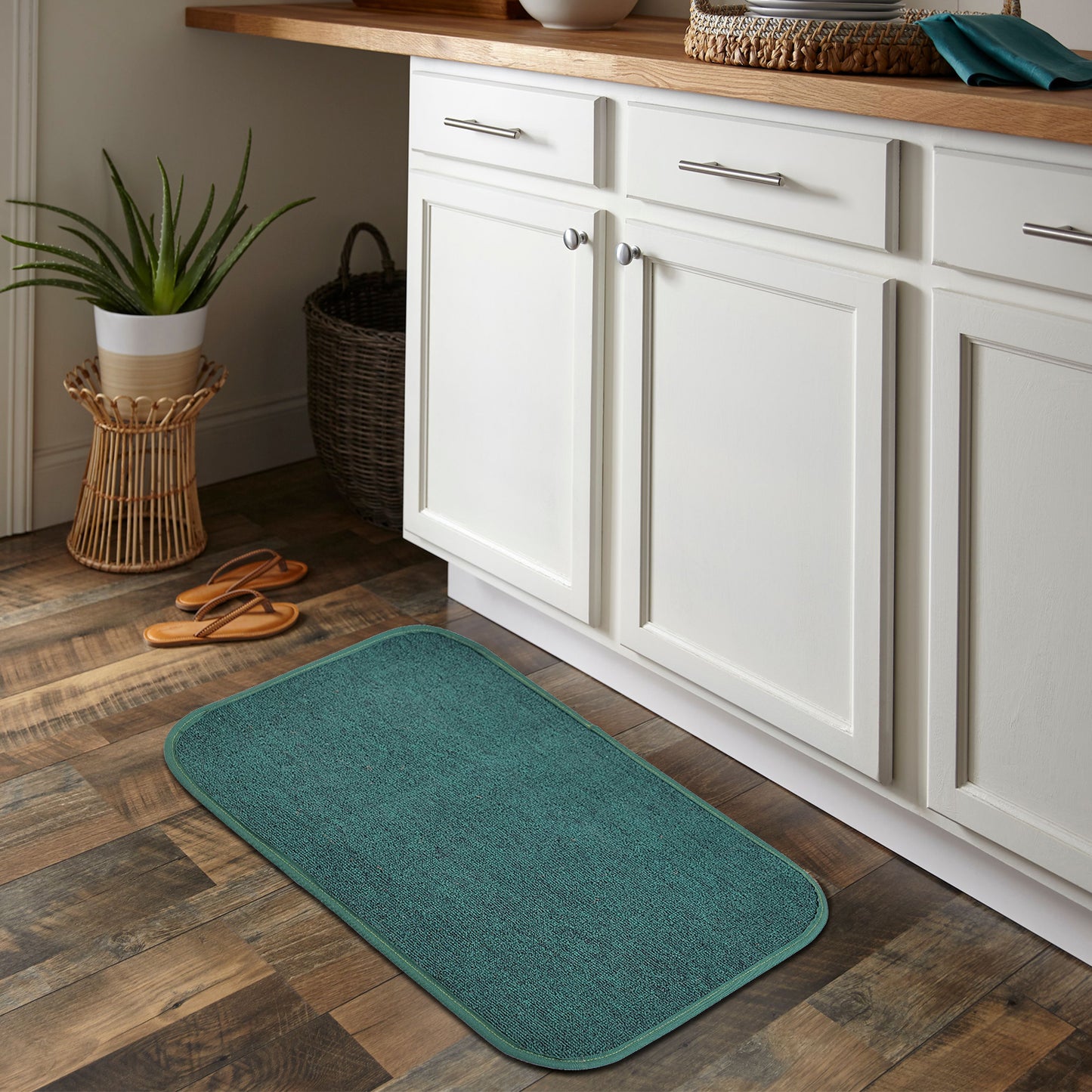 A green rectangular mat placed on a wooden floor, with a German flocked design, placed in a home setting near a kitchen counter.