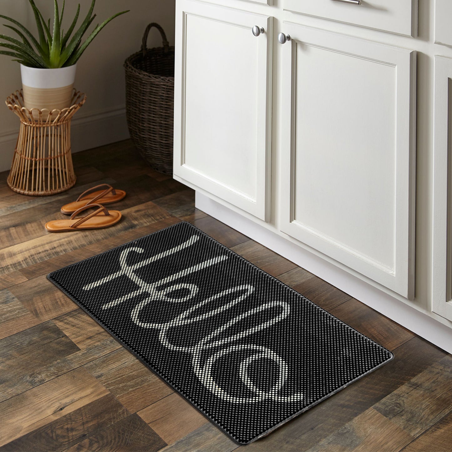 A black rectangular rubber floor mat with the word 'Hello' written in white, placed on a wooden floor in a home environment.