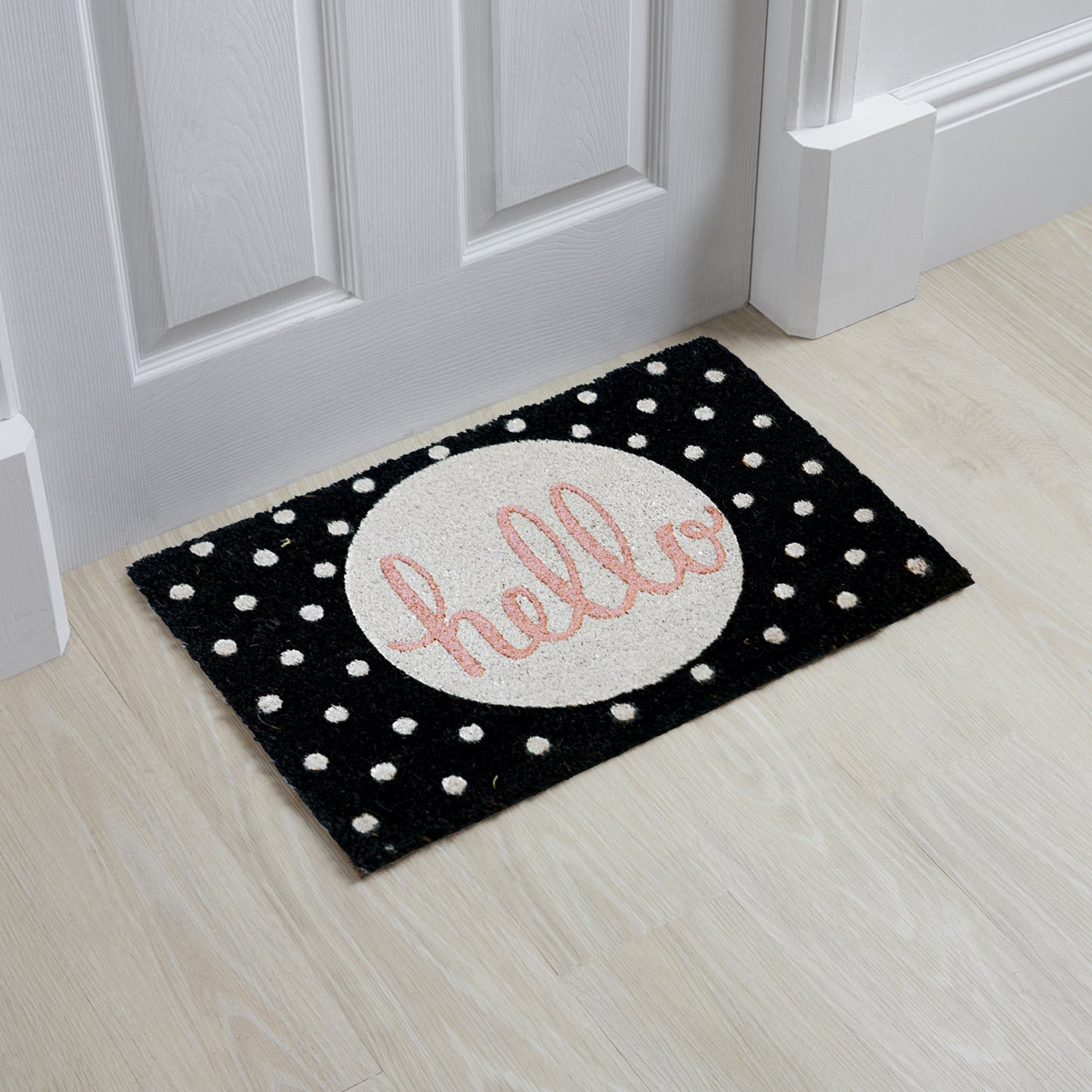 A rectangular, black and white coir floor mat with the word 'HELLO' written in glitter, placed on a light wooden floor.