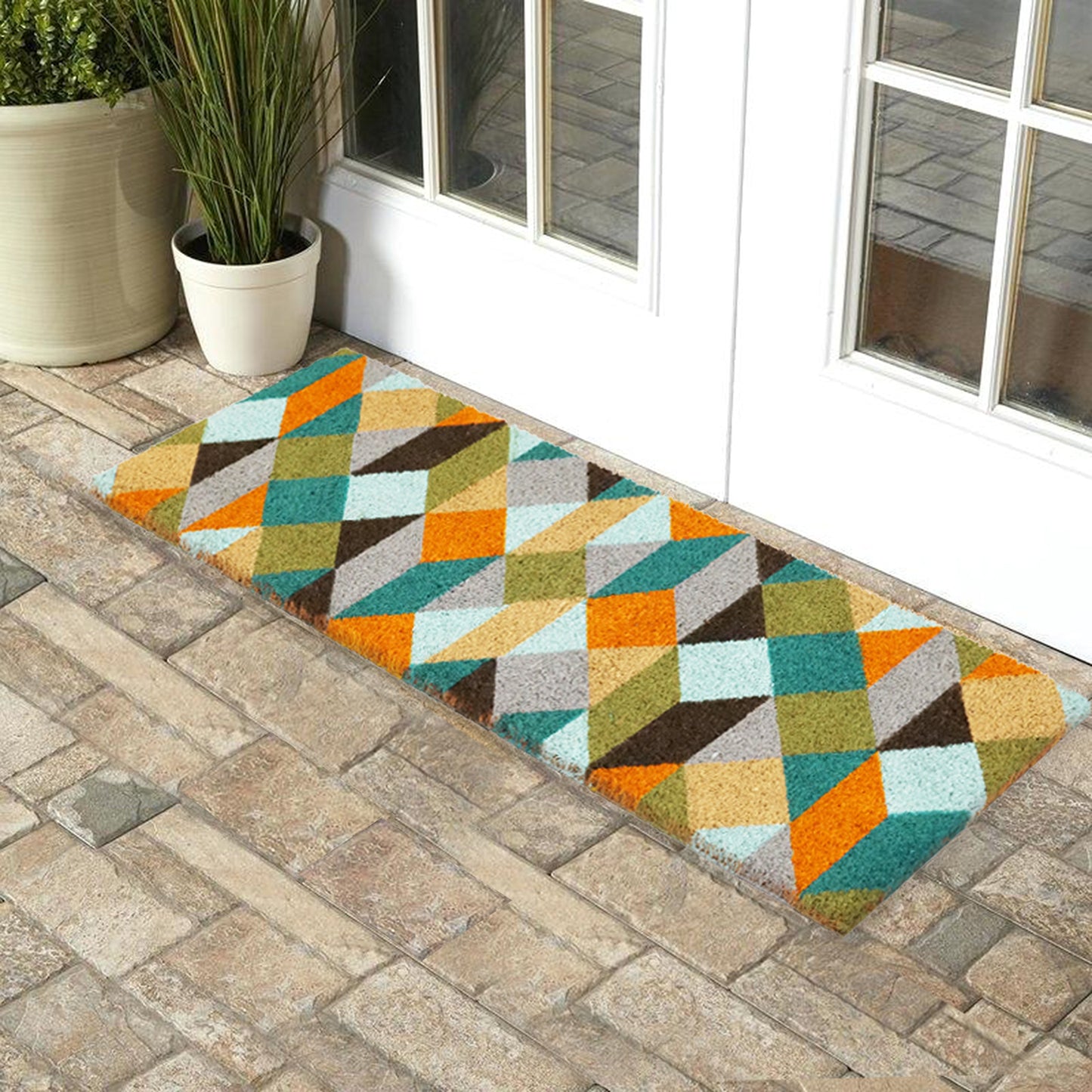 A rectangular, multicoloured, geometric-patterned coir floor mat with PVC backing is placed on a doorstep.