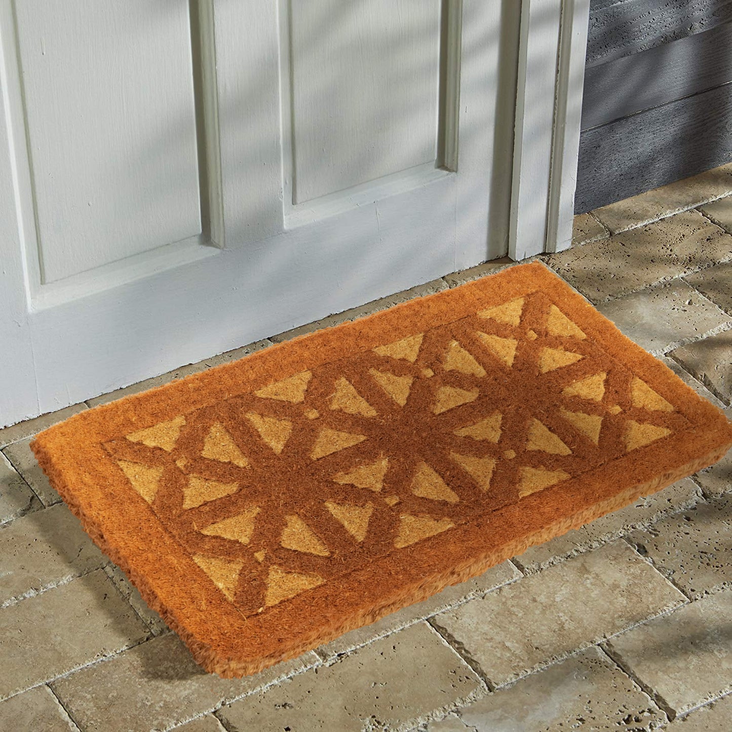 A rectangular coir door mat with a geometric hand-inlaid design is placed on a doorstep.