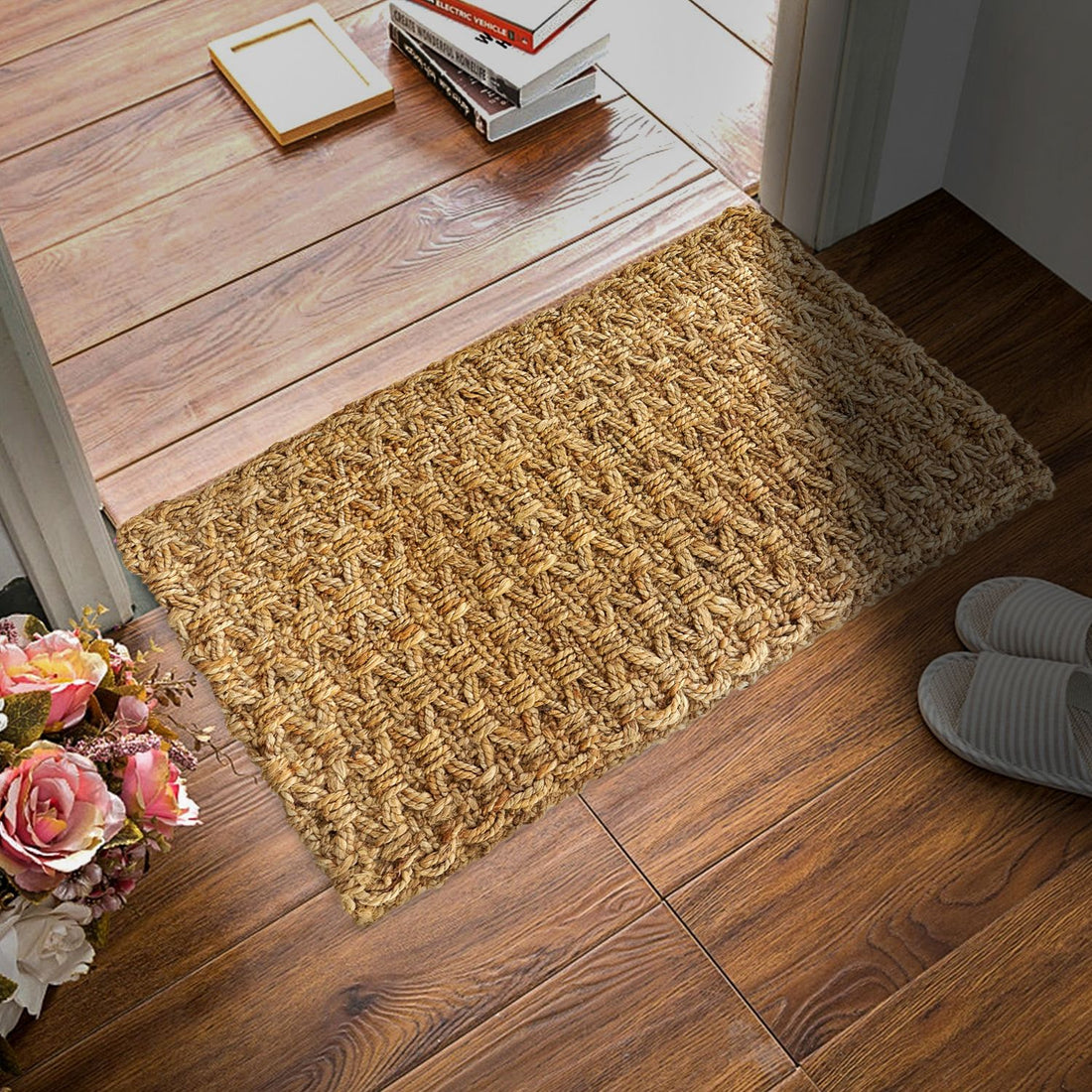 A beige braided and knotted jute mat is placed on a wooden floor, with a wooden door in the background and a pair of shoes to the side.
