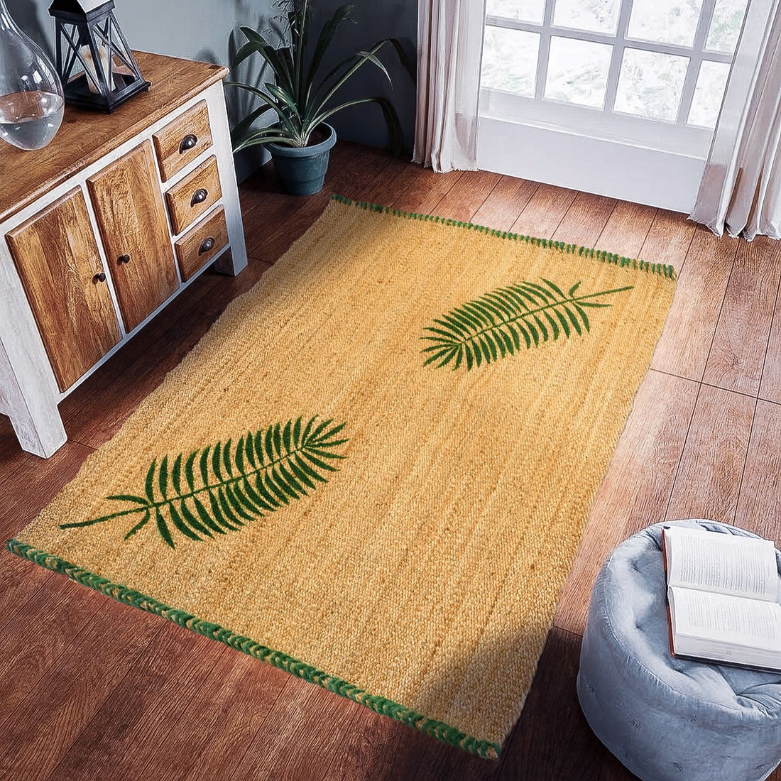A rectangular jute rug with a design of palm leaves in green on a yellow background, placed on a wooden floor in a room with a wooden cabinet, a potted plant, and a blue cushion.
