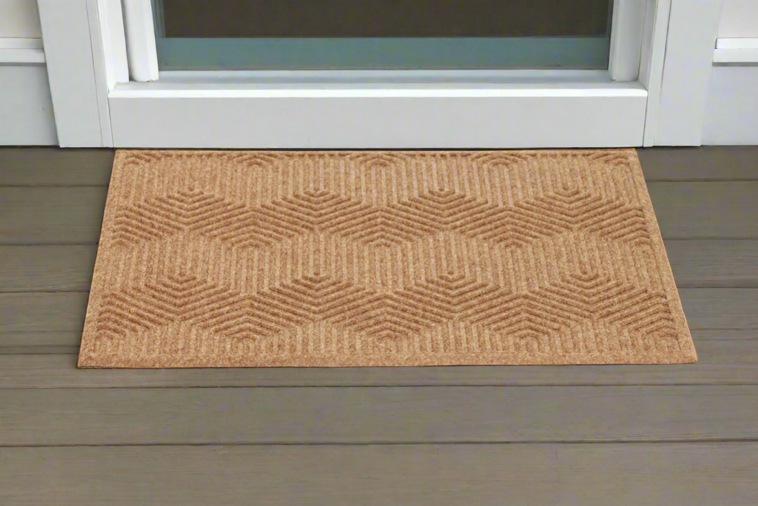 A rectangular, beige entry doormat with a geometric pattern, placed on a wooden doorstep.