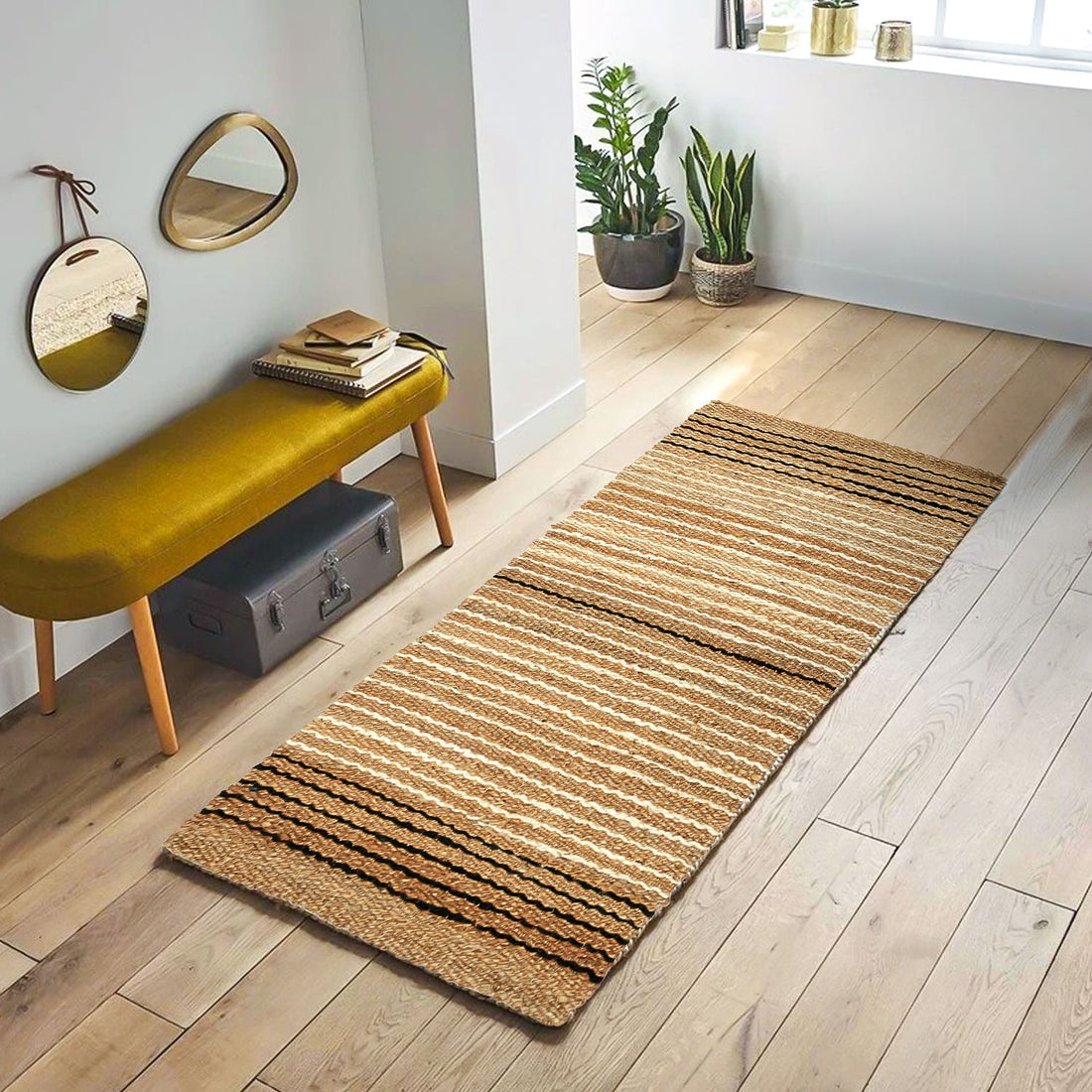 A rectangular, flat-weave jute rug with horizontal stripes, placed on a wooden floor in a living room setting with a yellow bench, a plant, and a mirror in the background.