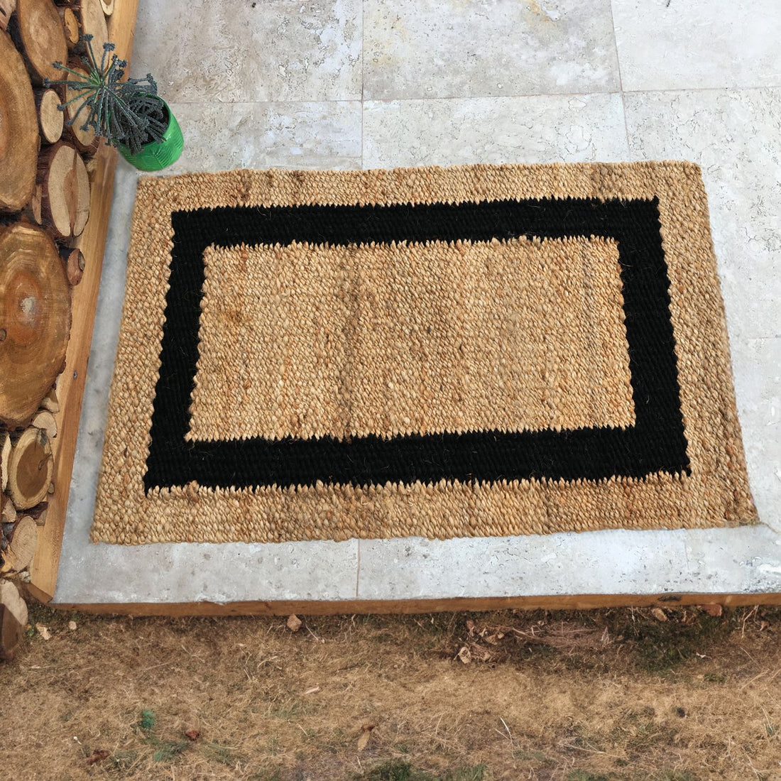 A beige handwoven jute rug with a black border, placed on a tiled floor step, with a wooden log step and a plant beside it.