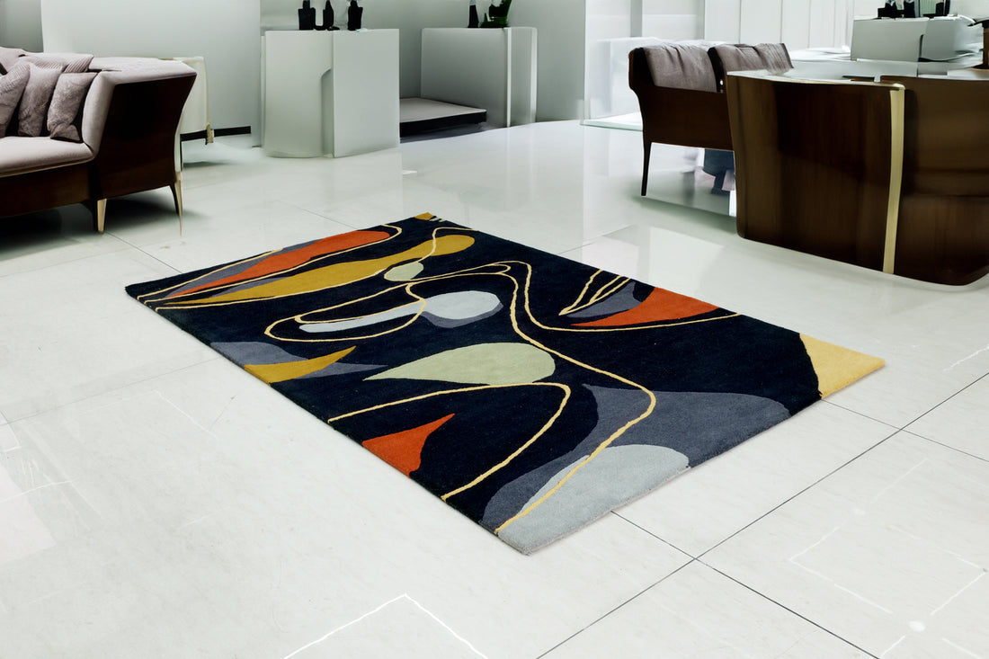 A modern geometric-patterned Bamboo Silk rug featuring a mix of black, grey, and multicoloured design elements, placed on a light floor in a stylish indoor setting.