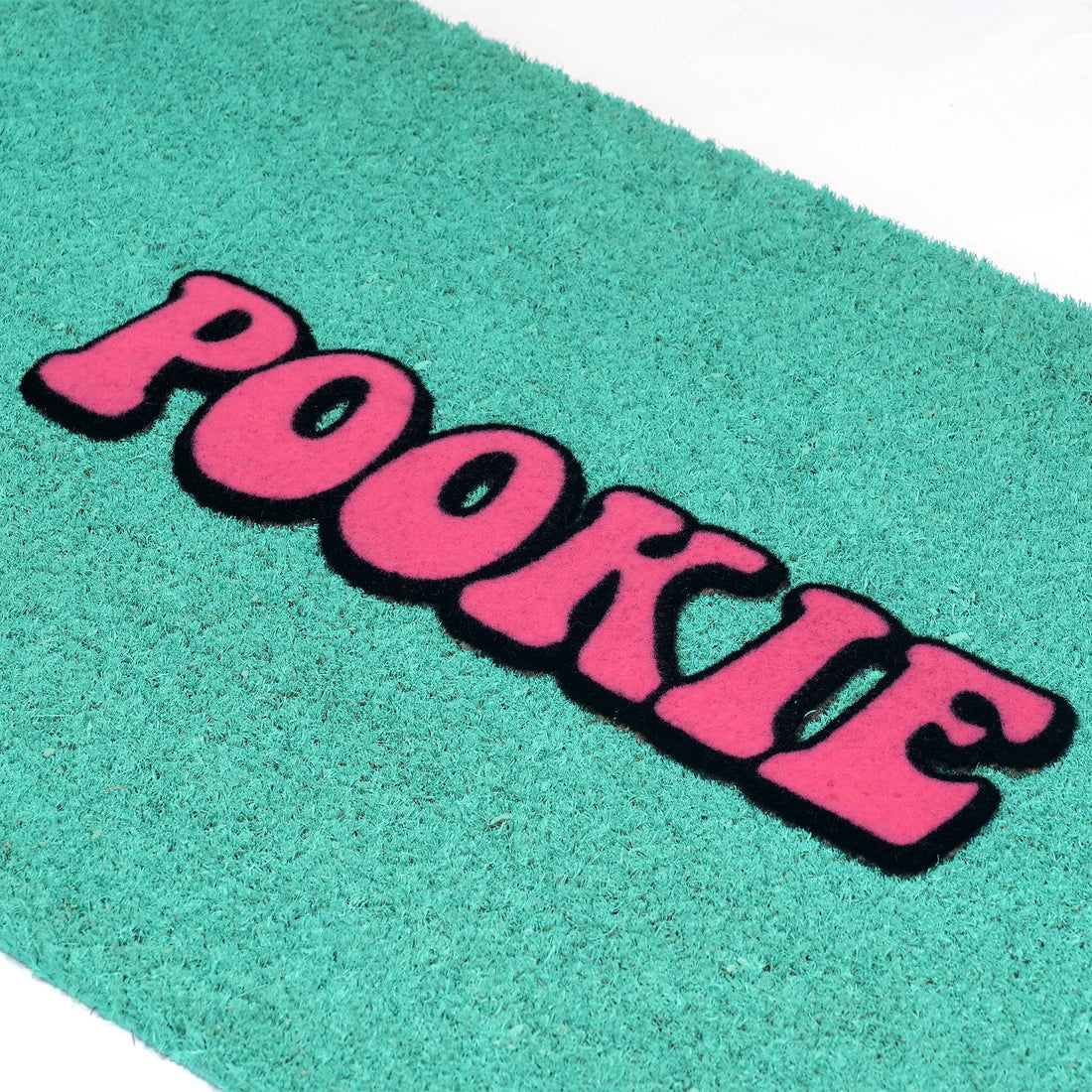 
                      
                        A close-up of a teal-green textured doormat with the word 'POOKIE' in bold pink letters outlined in black, placed on a white surface.
                      
                    