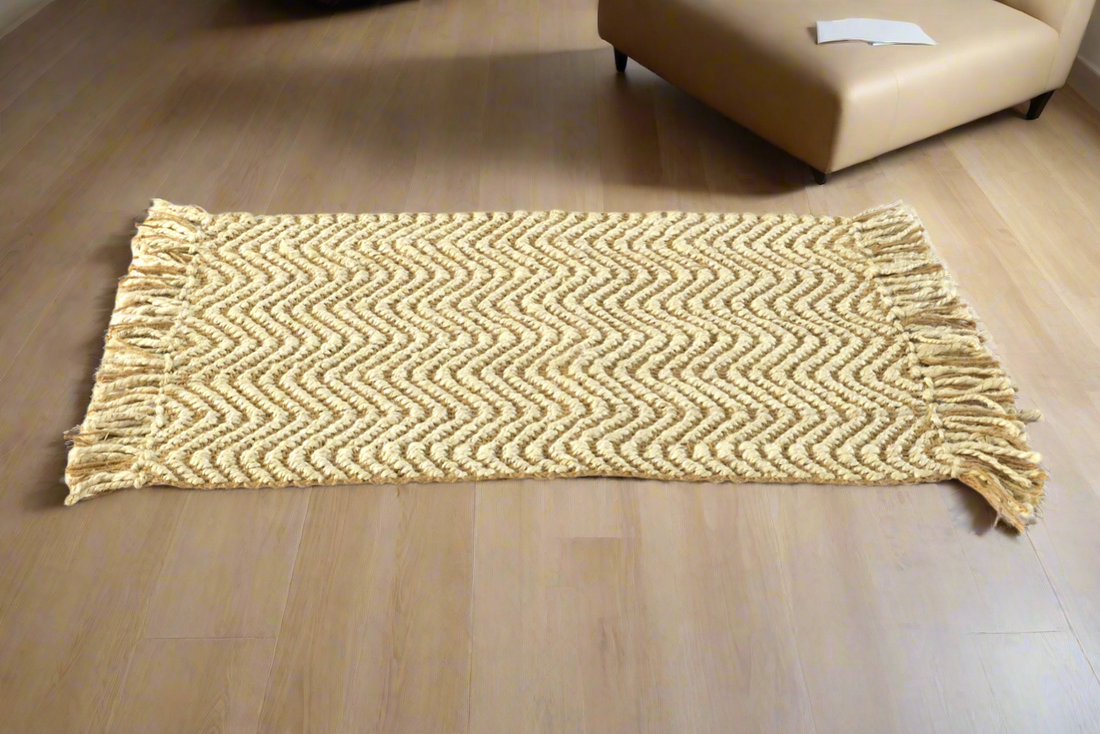 A beige hand-woven jute rug with a herringbone pattern placed on a wooden floor, with a couch and chair in the background.