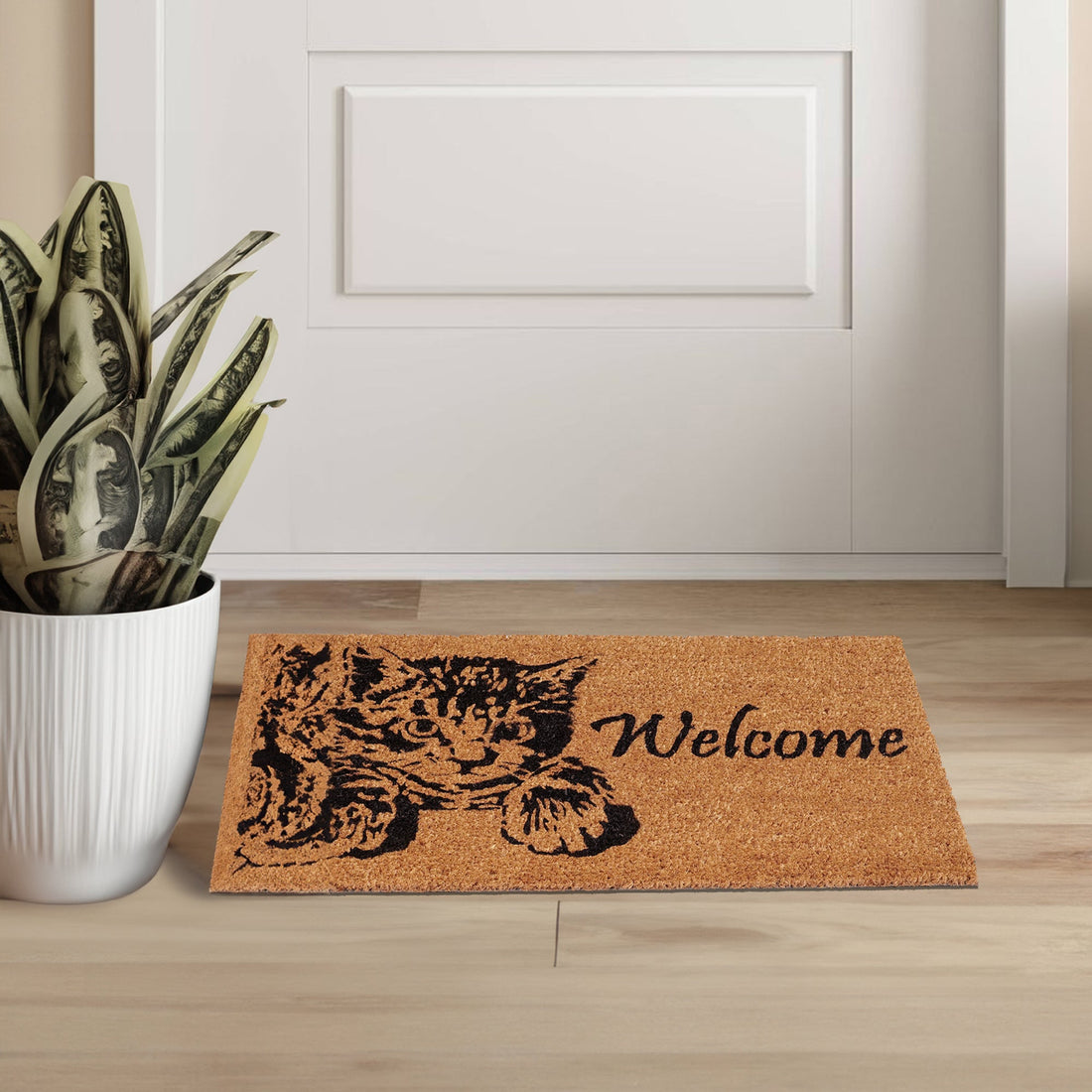 A rectangular natural coir doormat with a printed design of a black cat and the word 'WELCOME' on it, placed on a wooden floor in front of a white door.