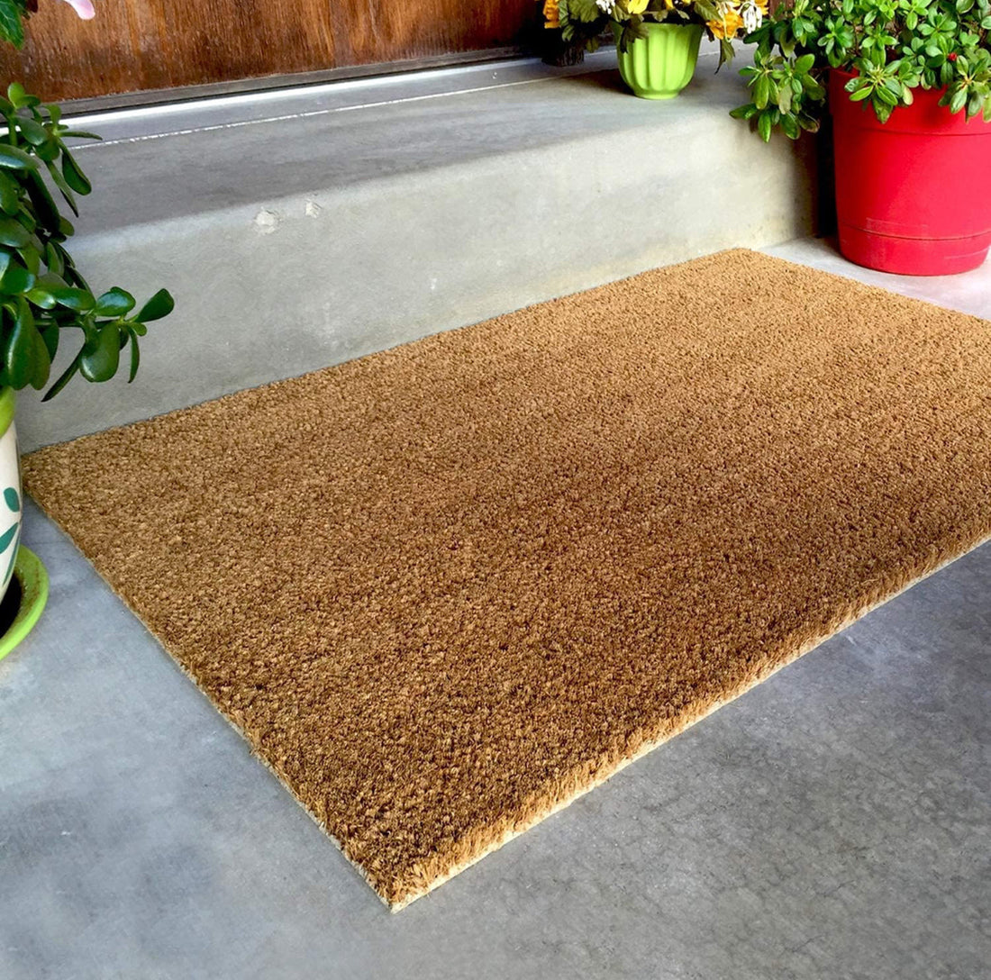 Brown plain coir doormat on a concrete floor with potted plants around