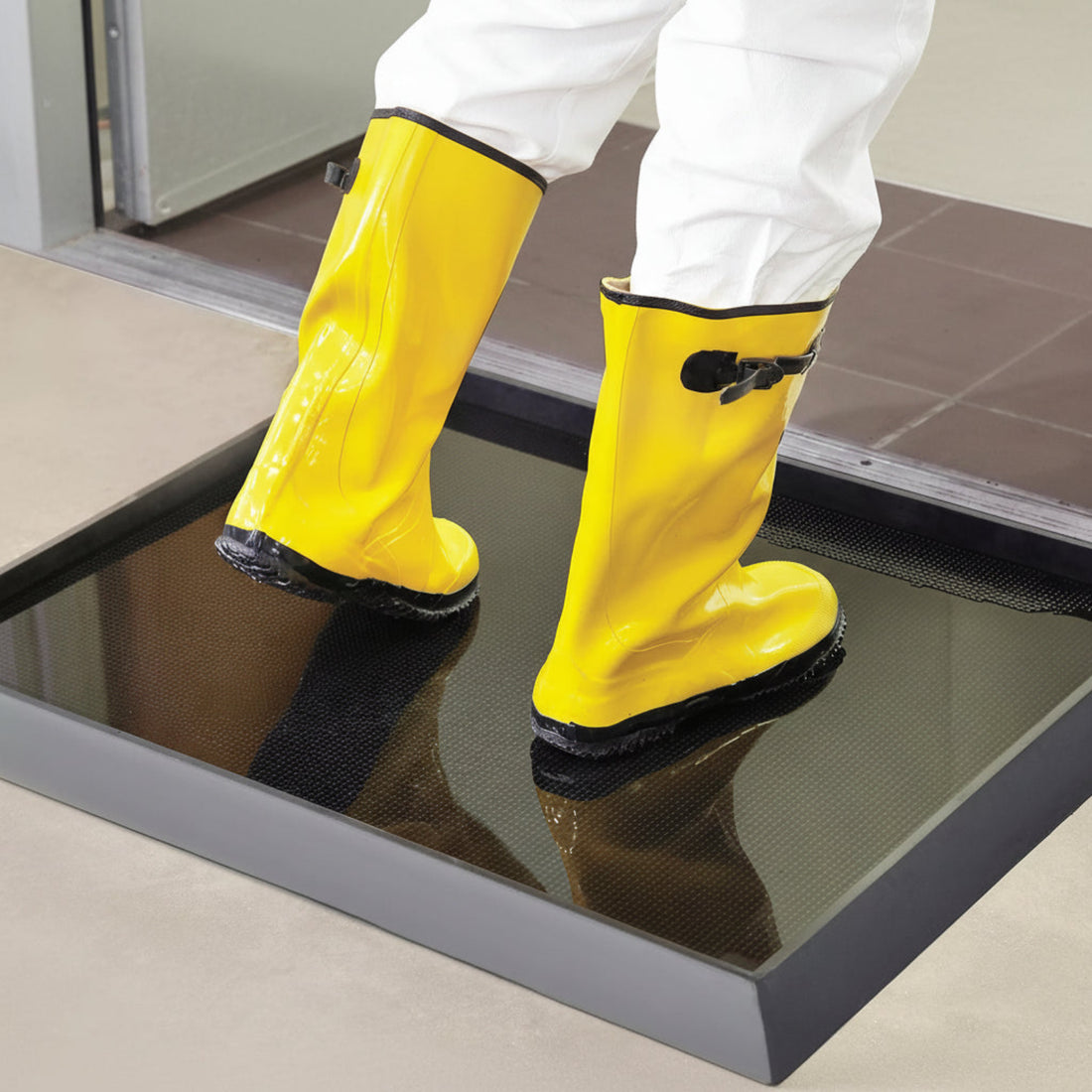 Yellow boots stepping onto a Rubber black floor mat with sanitize liquid