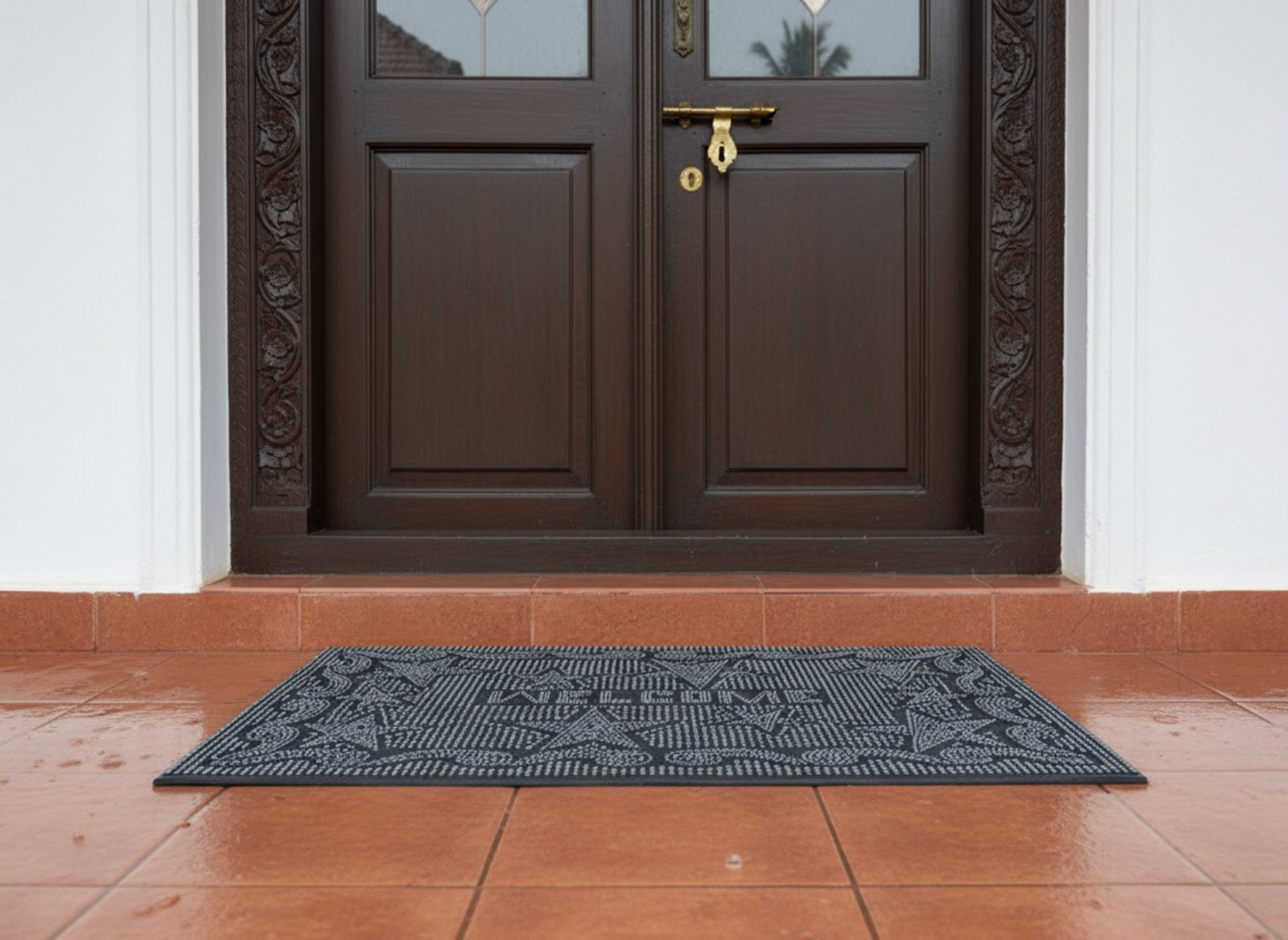 Black rubber pin doormat with a geometric pattern in front of a brown door