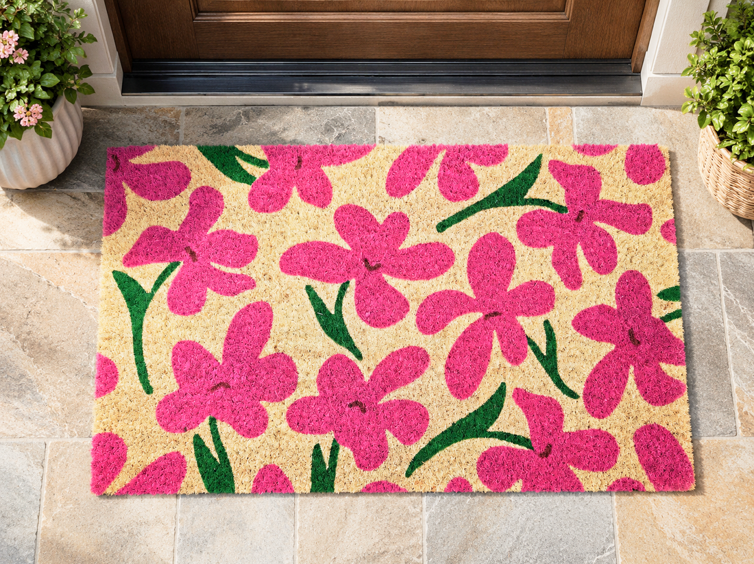 Floral doormat with pink flowers on a beige background, placed outside a door.