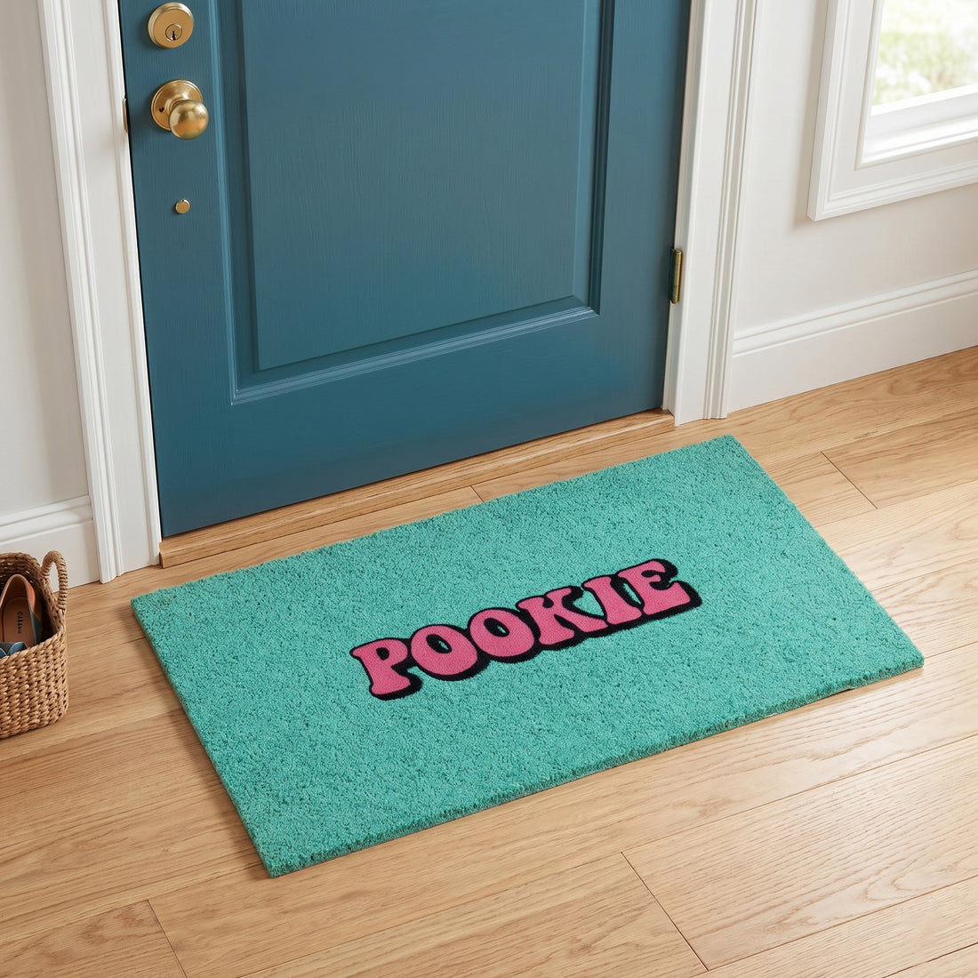 
                      
                        A teal rectangular doormat with the word 'POOKIE' in pink letters outlined in black, placed in front of a blue door on a light wood floor.
                      
                    