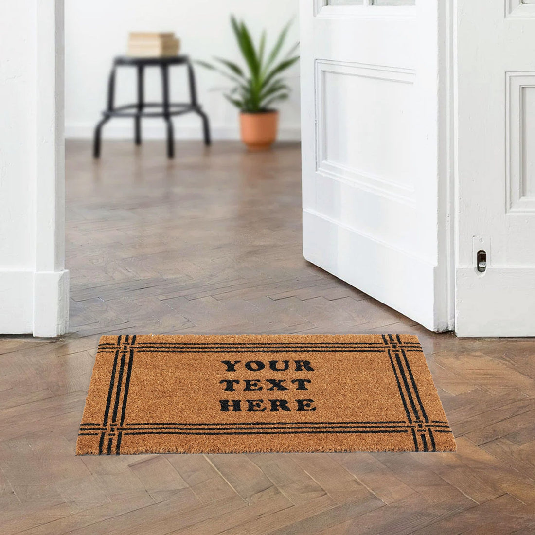 A personalized coir doormat with a double-line border design, placed on a floor matte, with a text 'YOUR TEXT HERE' printed on it, in a home environment.
