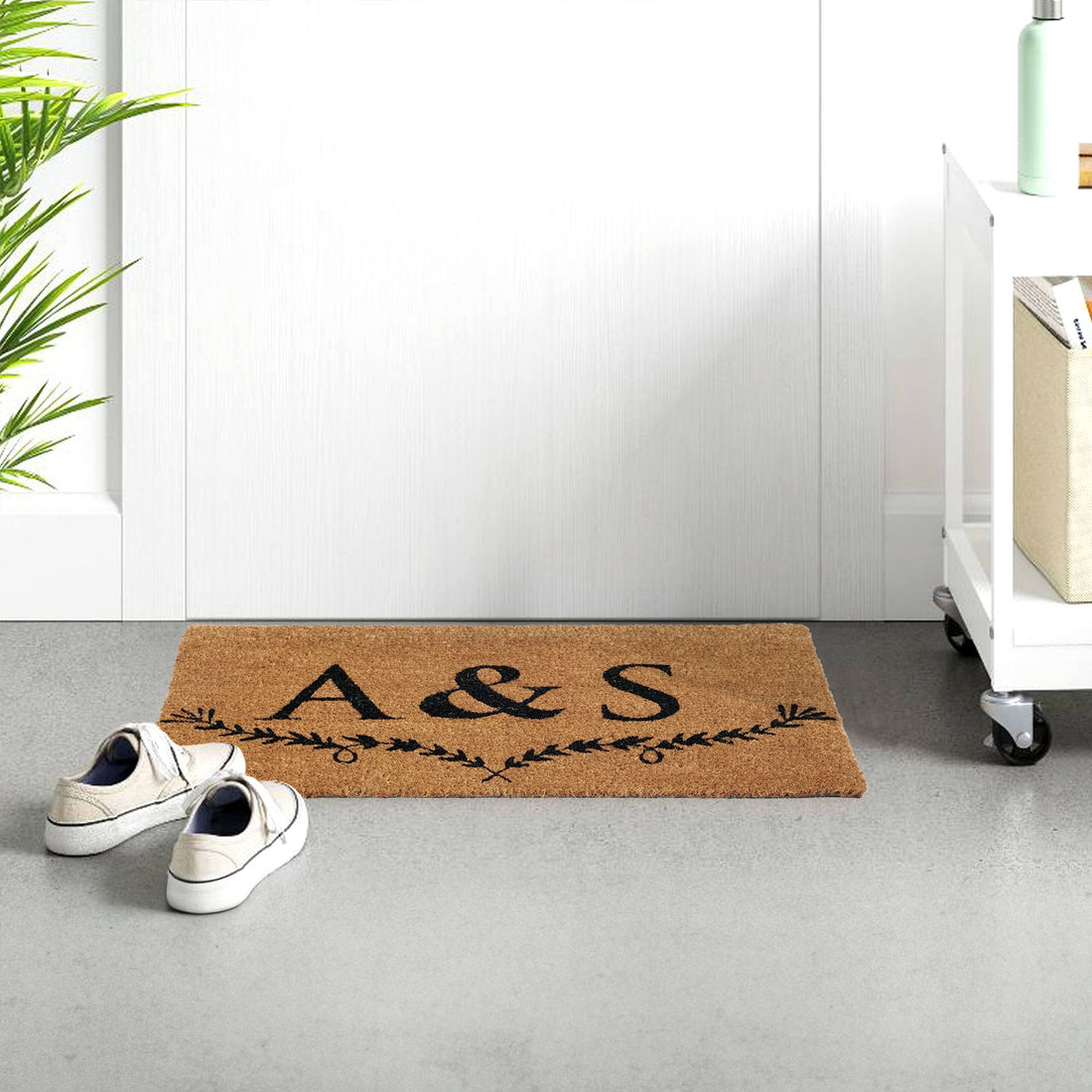 A personalised coir doormat with the initials 'A&S' embossed on it, placed on the floor next to a white door, with a pair of shoes at the bottom of the image.
