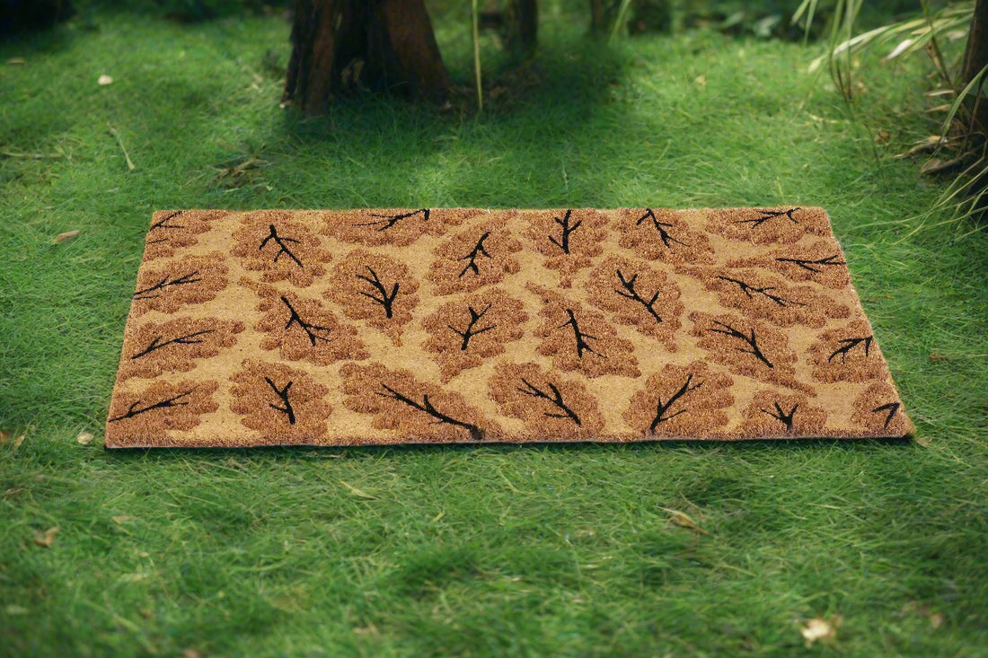 A beige coir mat with a leaf impression printed design, placed on a grassy surface.