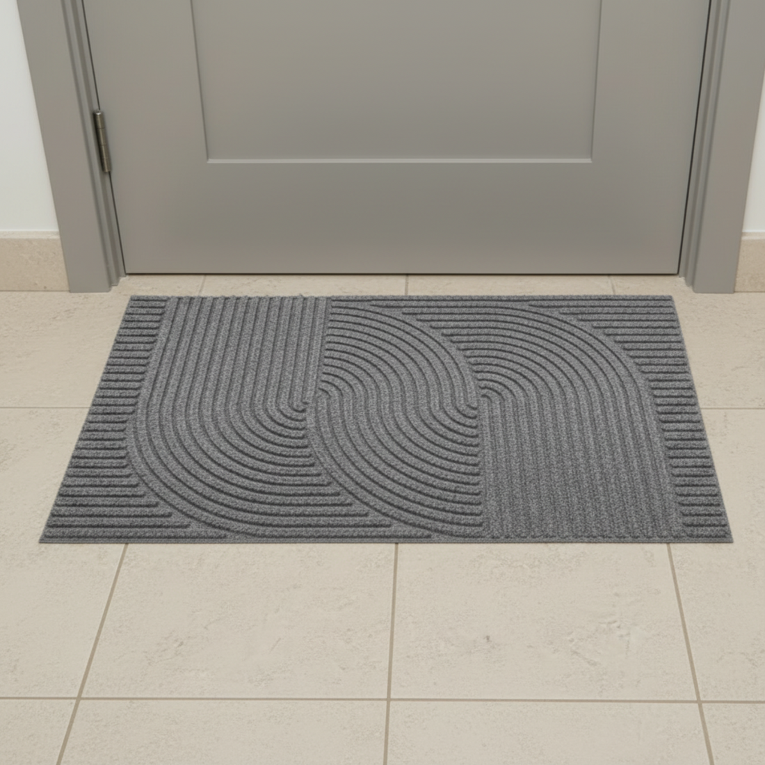 Gray doormat with a geometric pattern on a tiled floor in front of a gray door.