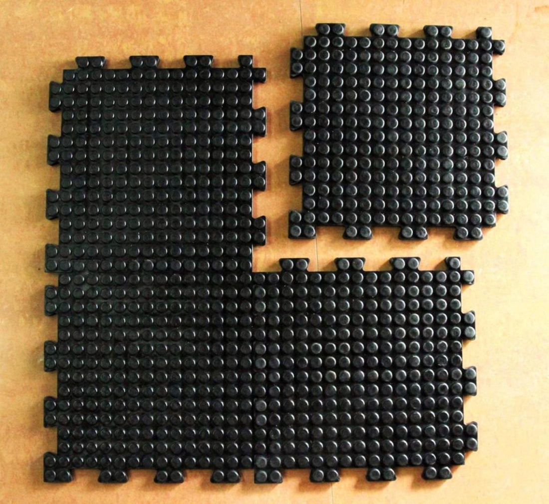 Interlocking black rubber floor mats arranged in a pattern on a brown surface.