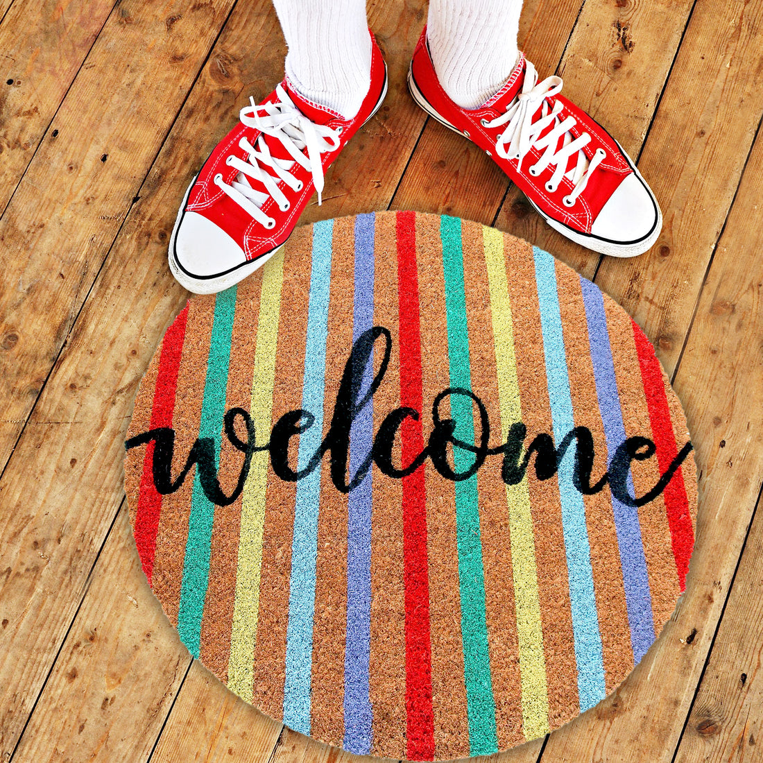 A round, colourful doormat with the word 'WELCOME' printed on it, accompanied by a pair of sneakers stepping on the mat.